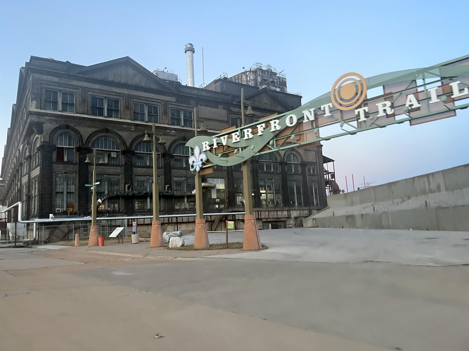 A large, old building next to a trail entrance sign on a paved area.