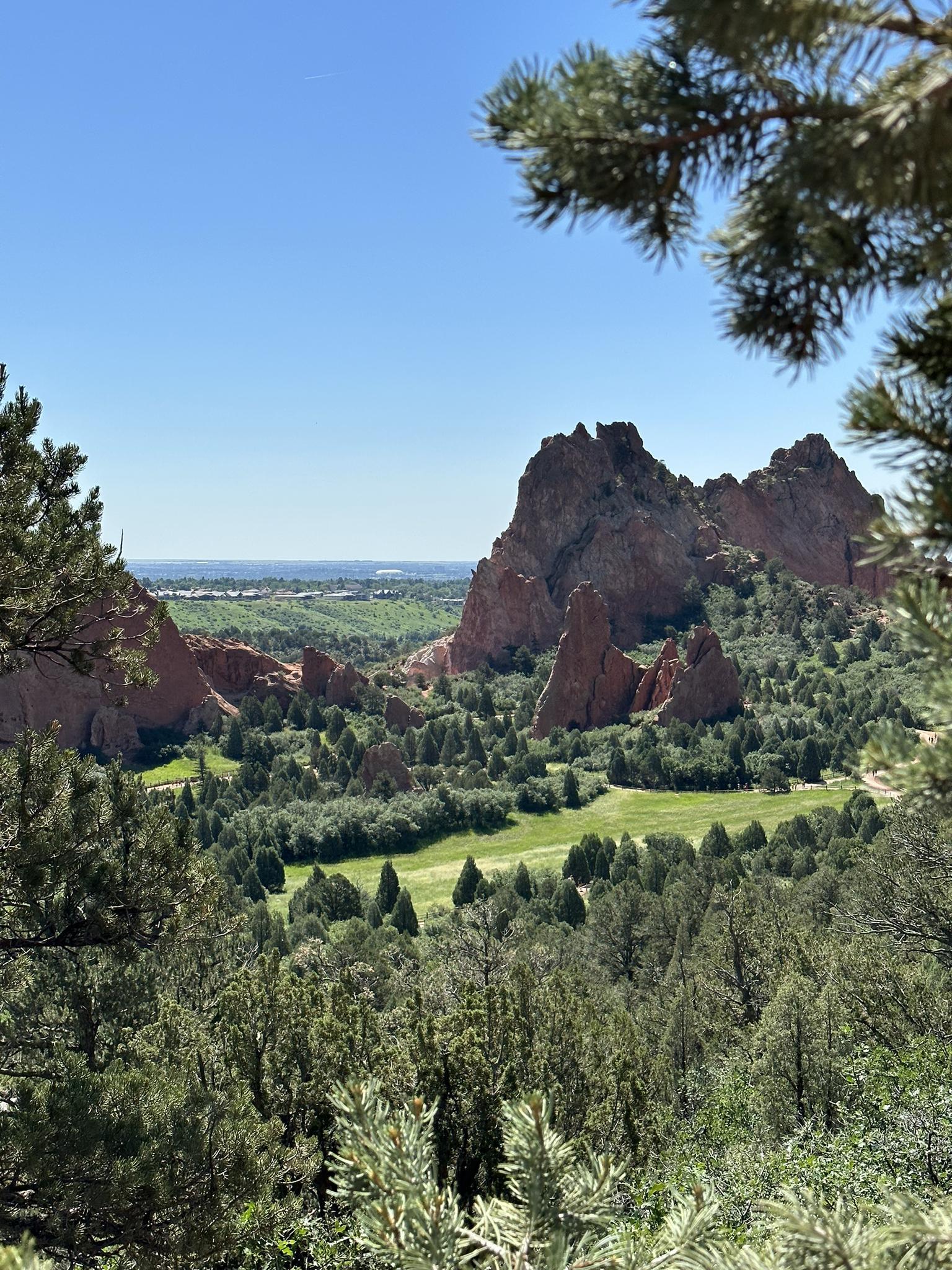 Expansive view of red rock formations, lush green fields, and dense trees.