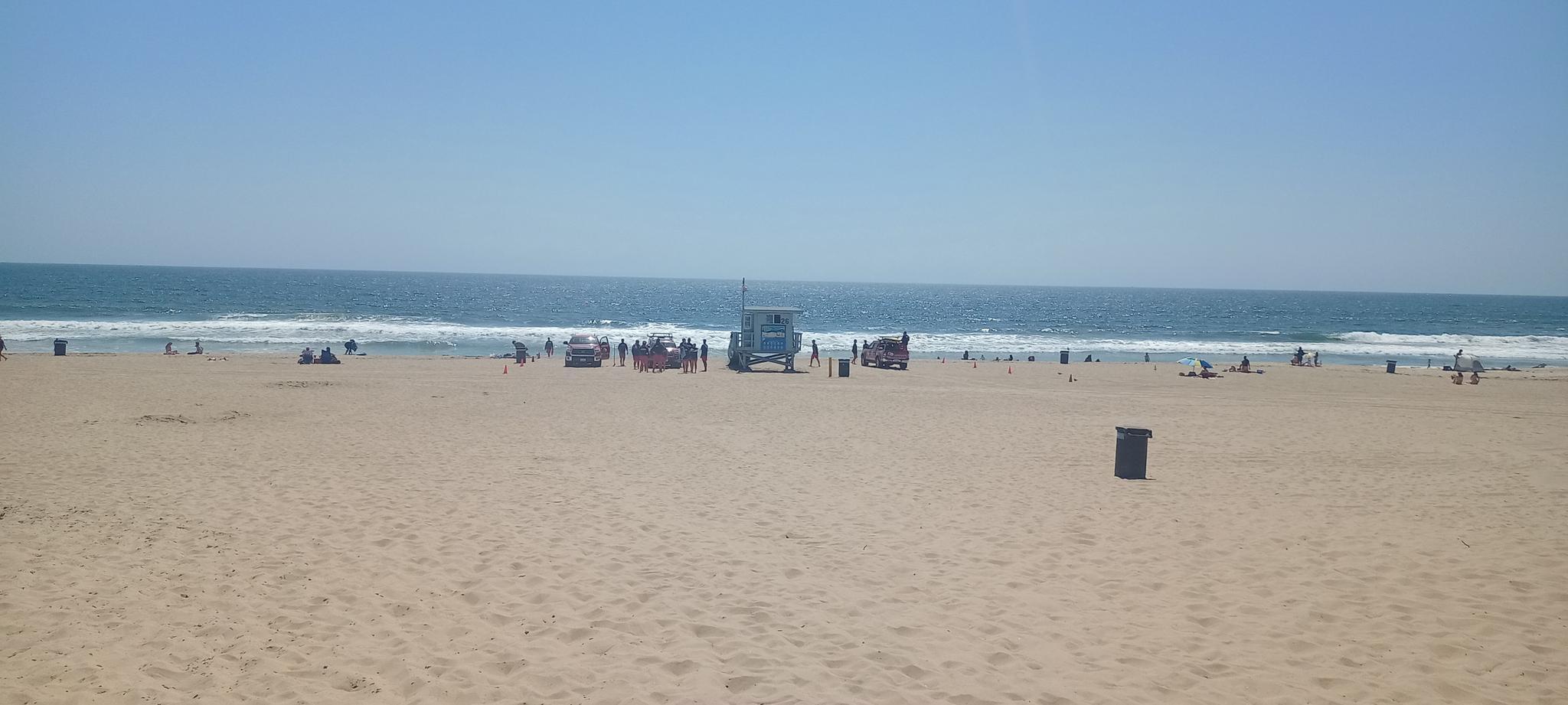 Sunny beach scene with ocean, lifeguard tower, and people enjoying the sand.