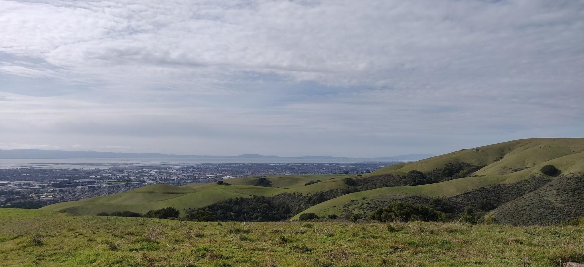 Expansive view of rolling green hills, a distant city, and water under cloudy skies. - Tolman Peak and South Fork Loop
