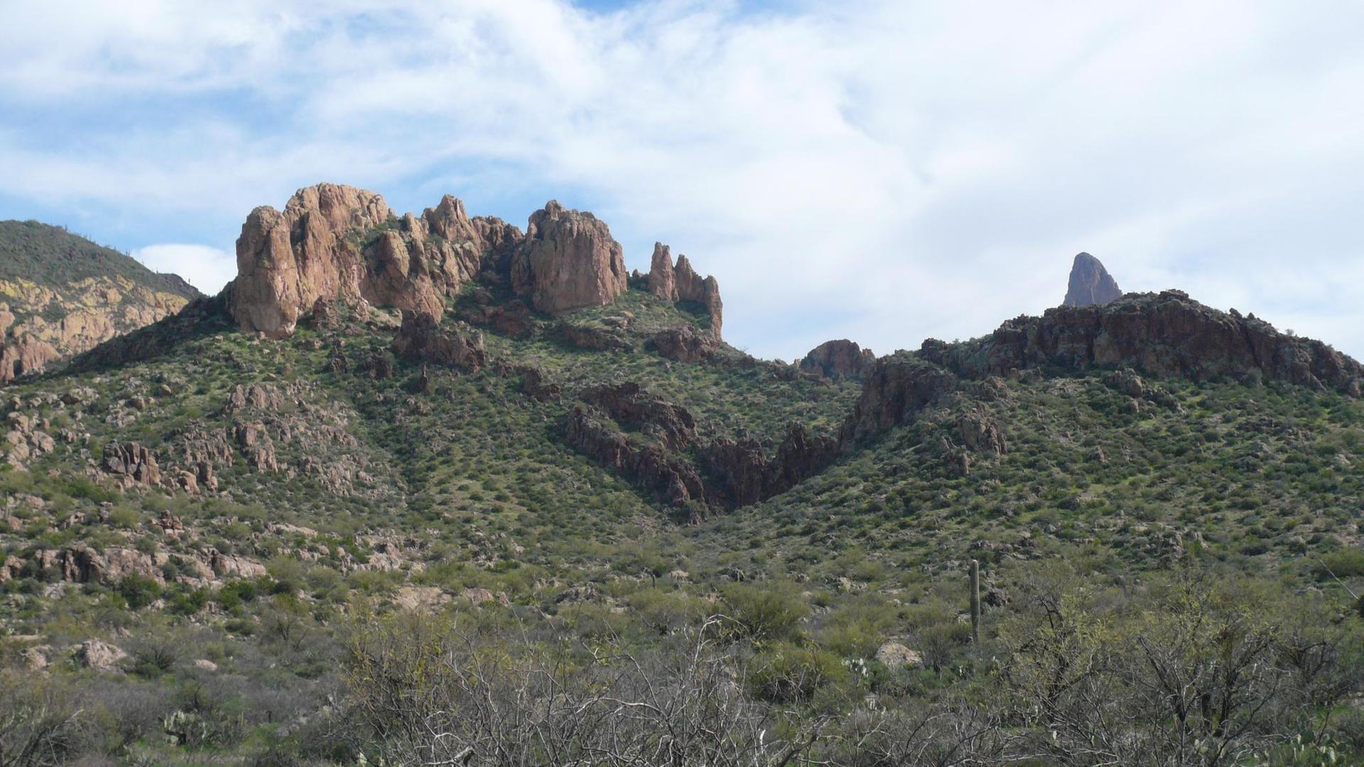 Rugged, rocky desert mountains covered in green scrub under a partly cloudy sky.