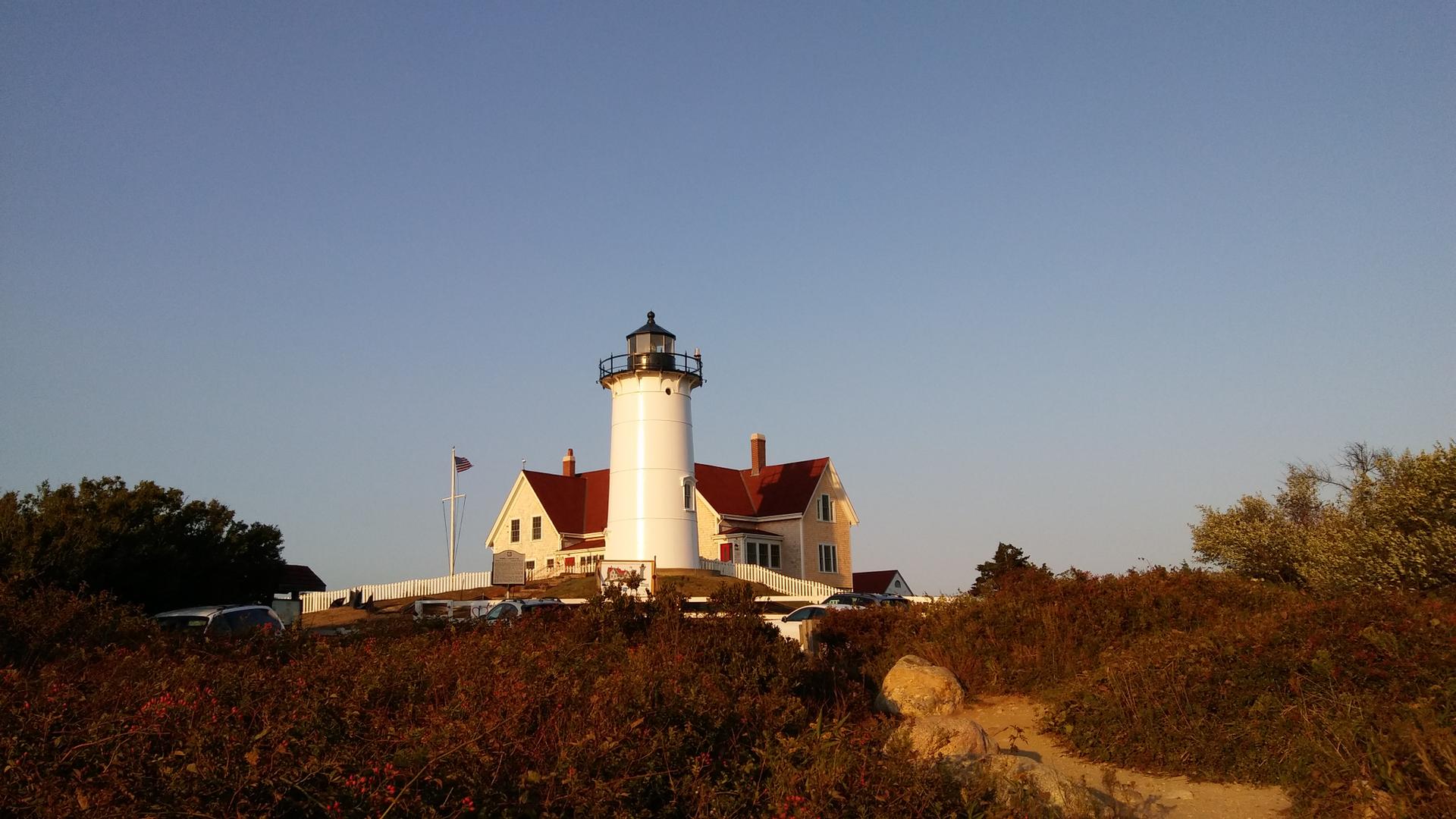 White lighthouse and house on a hill, bathed in warm golden hour light.