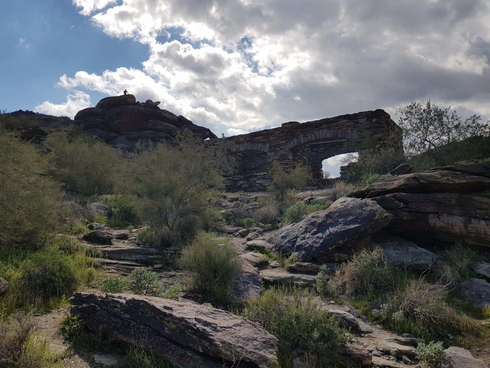 Ancient stone structure nestled in rocky desert hills under a cloudy sky.