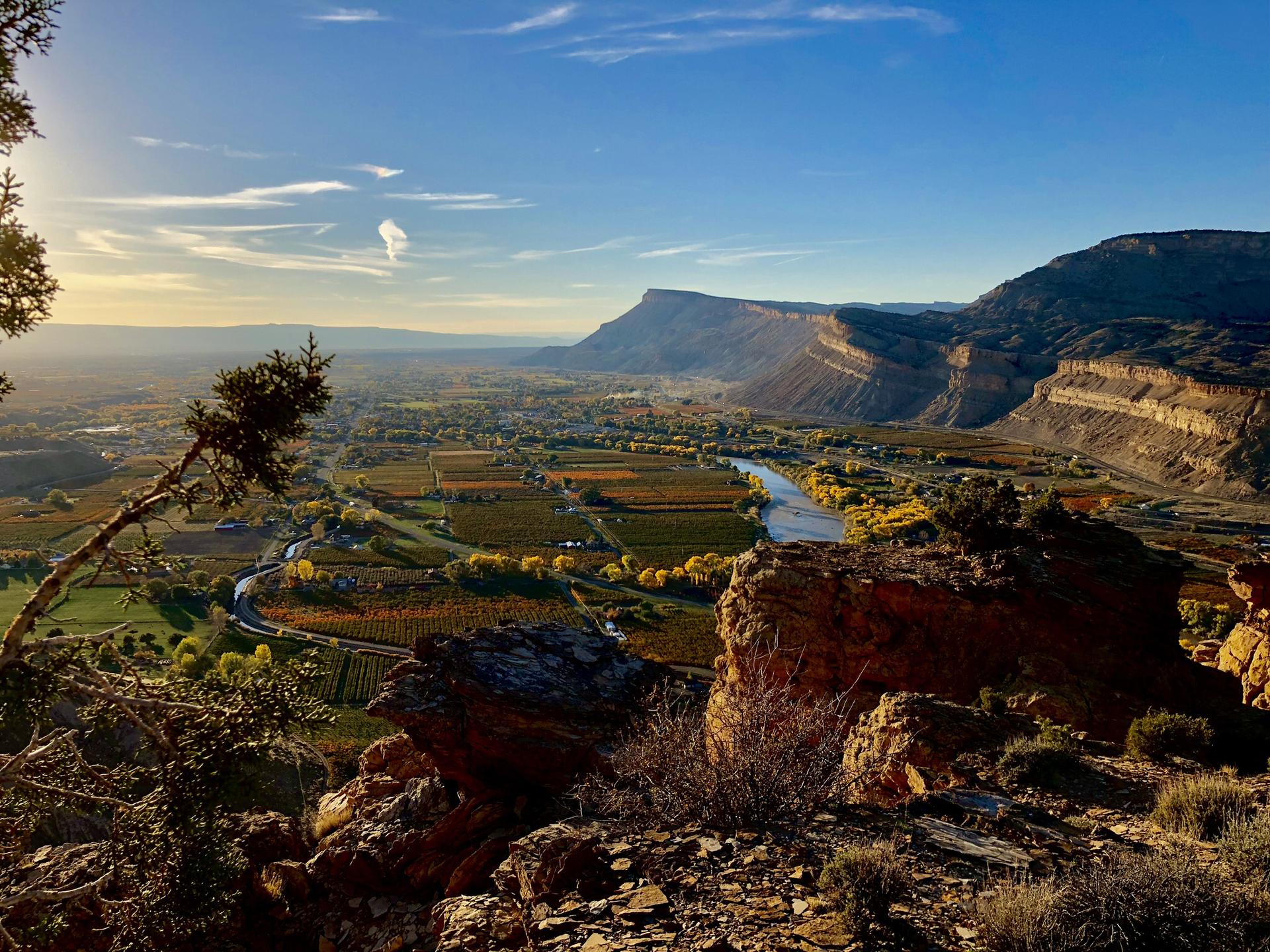 Golden hour light illuminates a wide valley with a river and distant mountains.