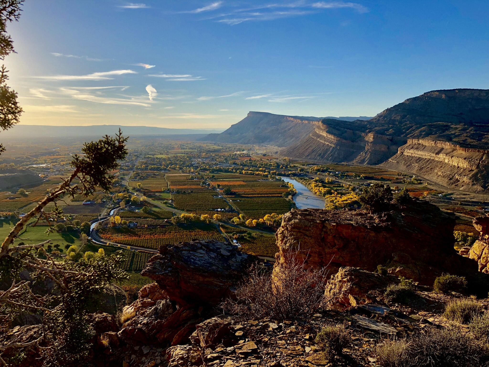 Golden hour light illuminates a wide valley with a river and distant mountains. - Palisade Rim Trail