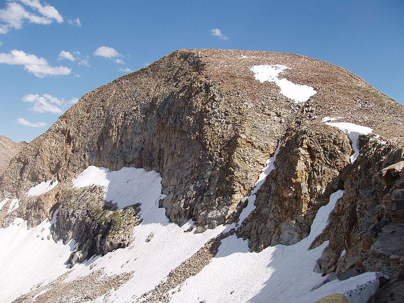 Rugged mountain peak with patches of snow under a bright blue sky.