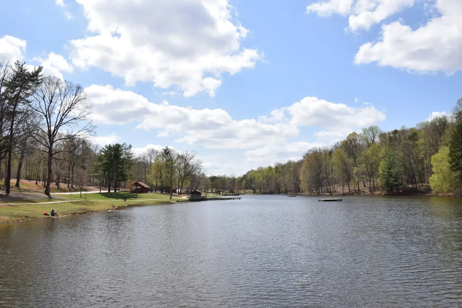 Wide lake surrounded by green trees under a bright, cloudy sky with boats.