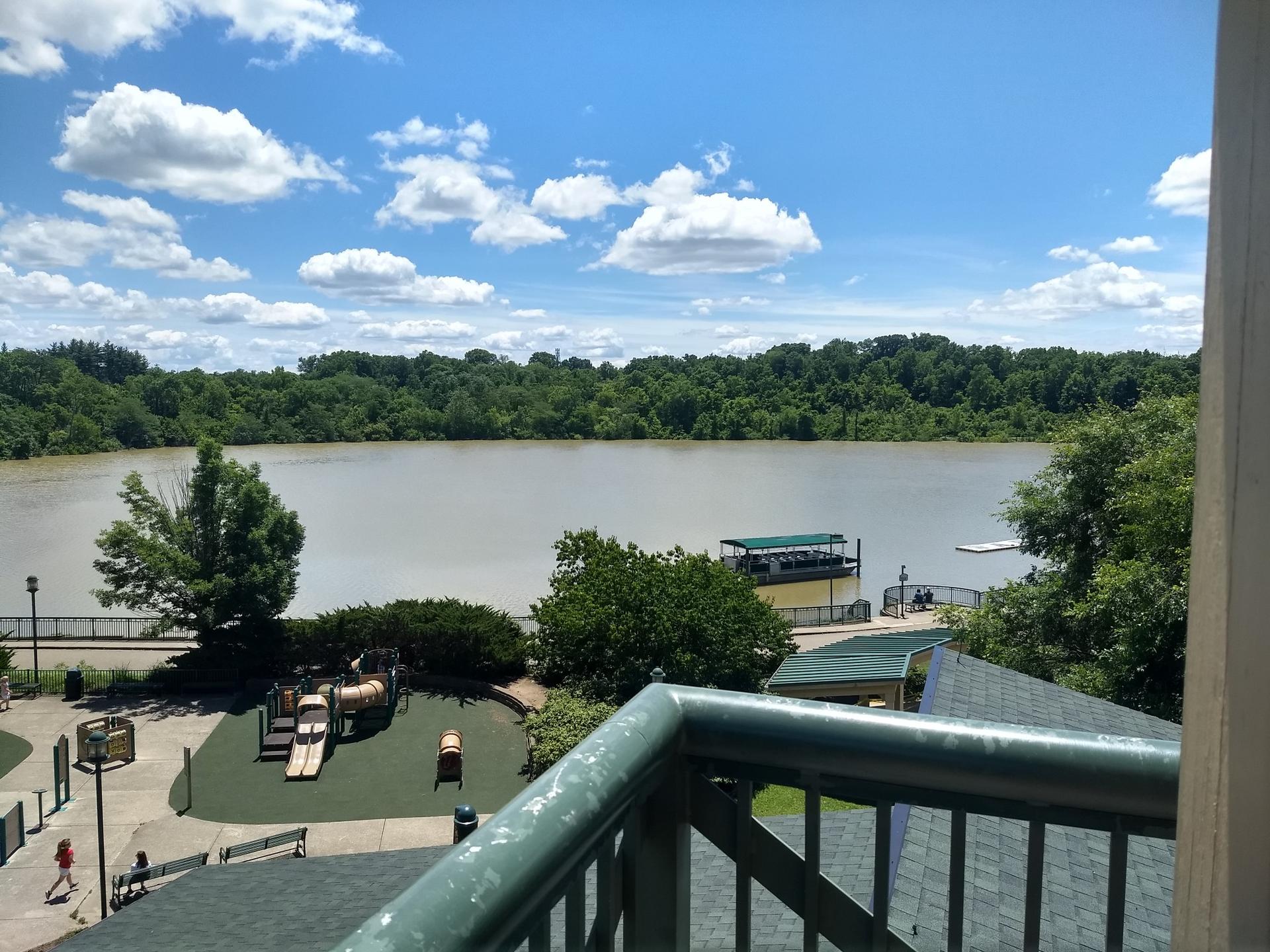 Overlooking a river, playground, and docks under a bright, cloudy sky.