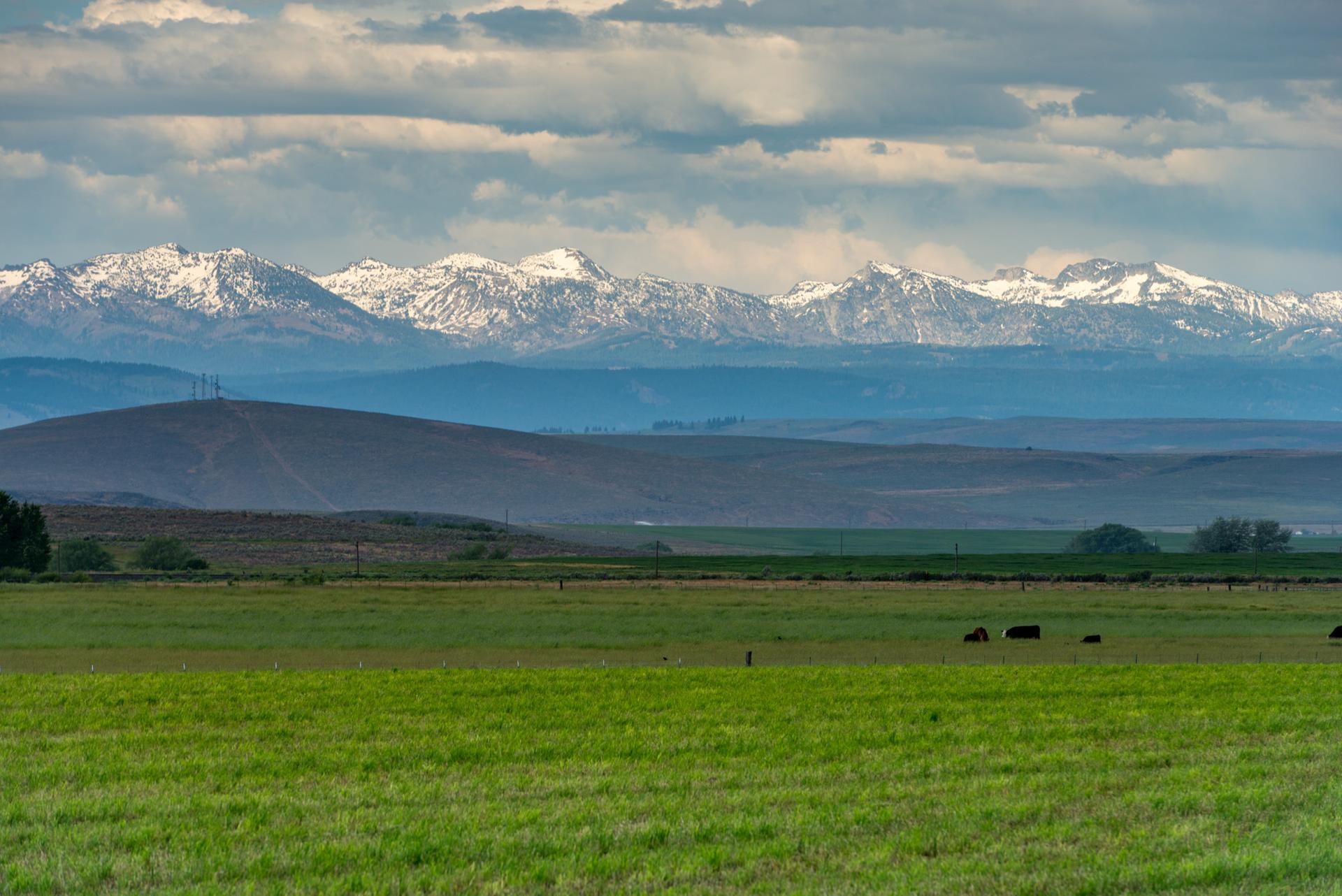 Snow-capped mountains rise above green fields under a cloudy sky.
