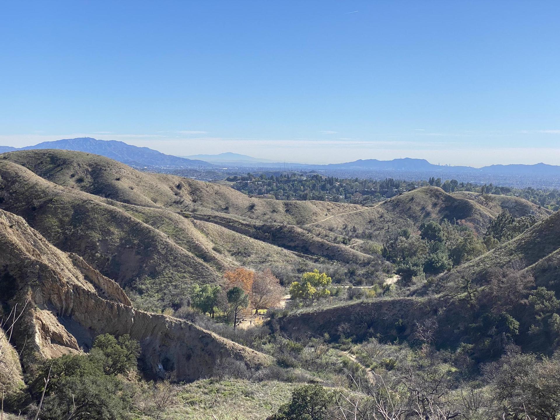 Panoramic view of dry rolling hills and a distant valley under clear skies.