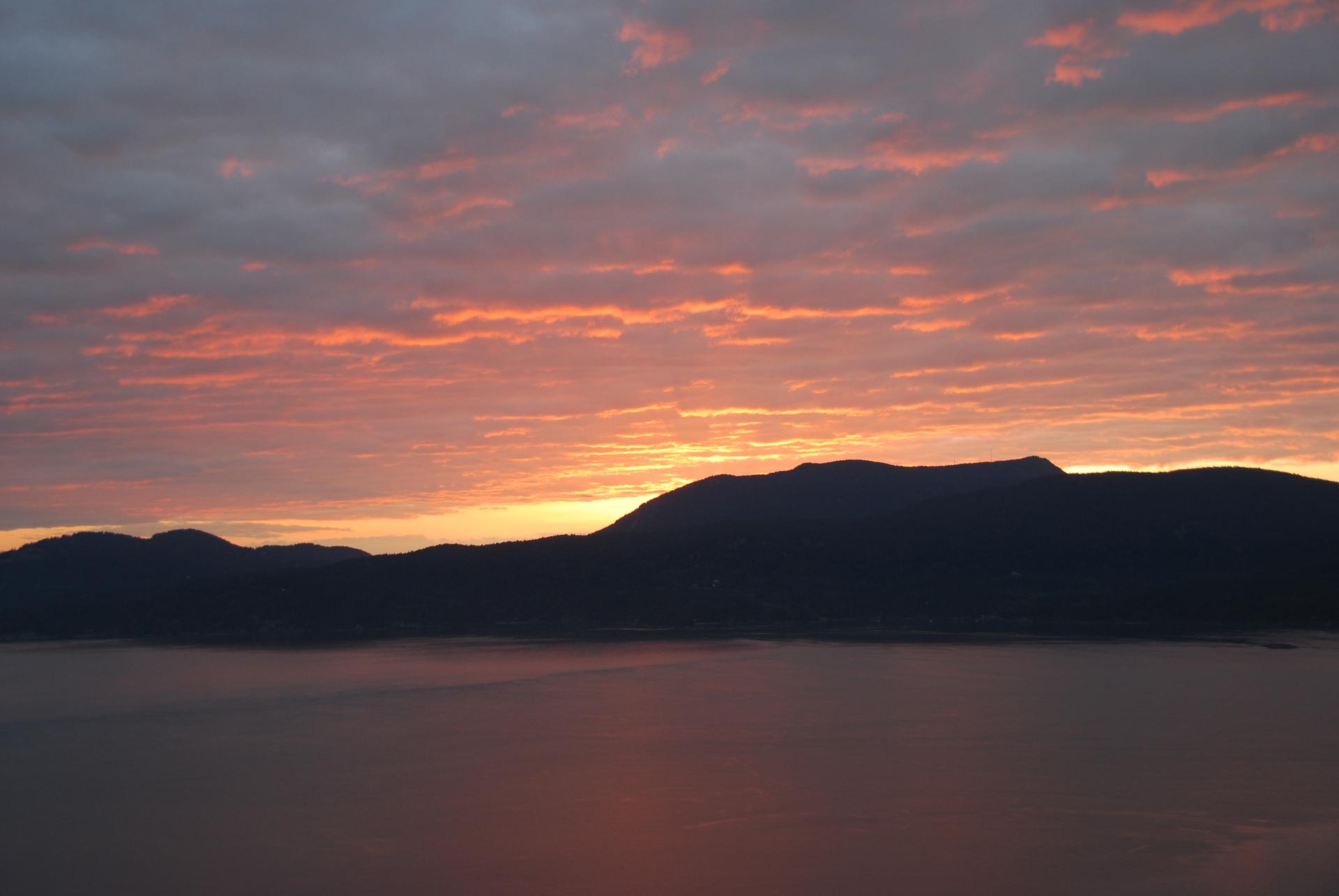 Vibrant orange and pink sunset over silhouetted mountains and calm water.