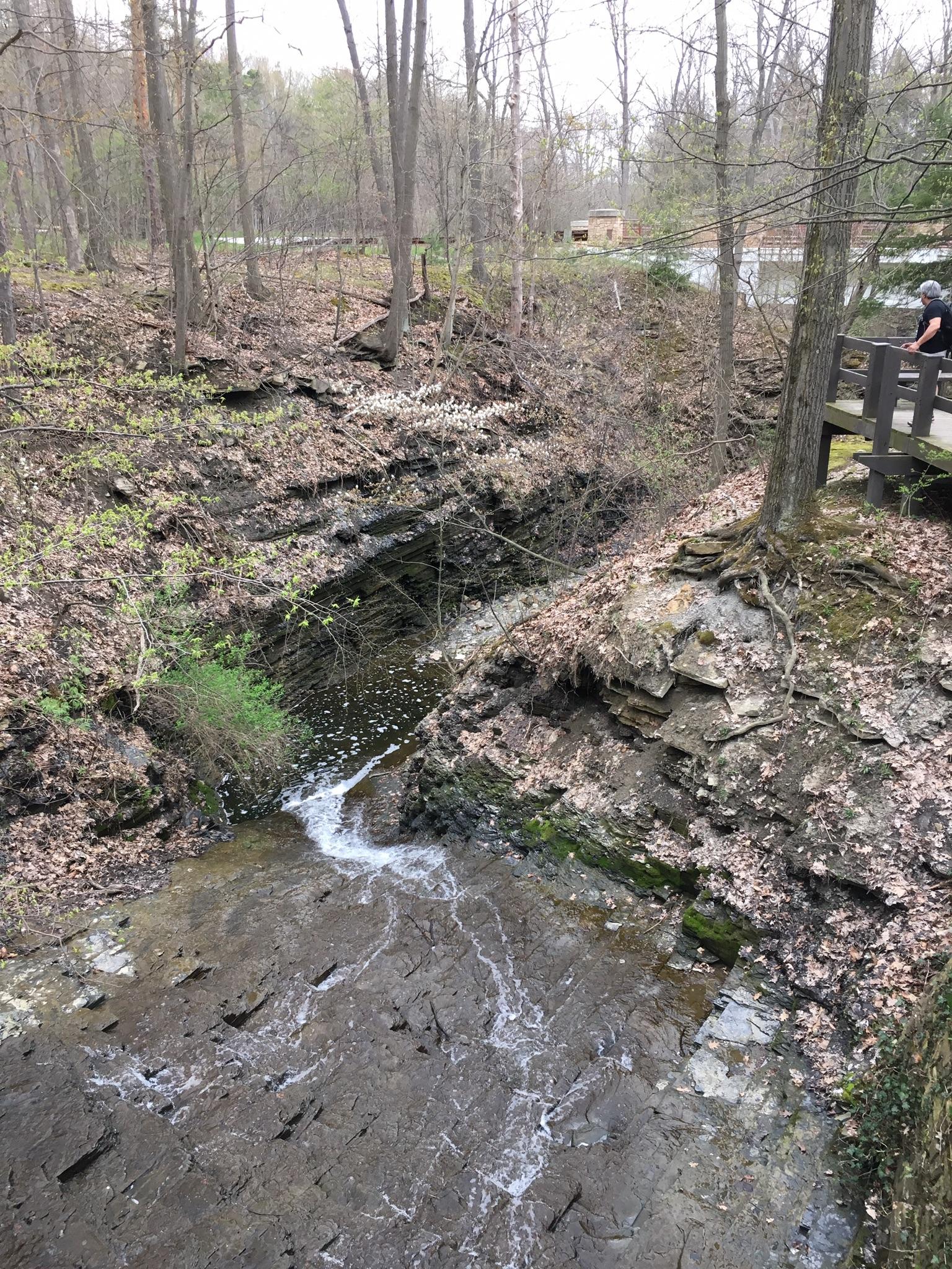Small waterfall cascading into a rocky gorge, with a person on a bridge.