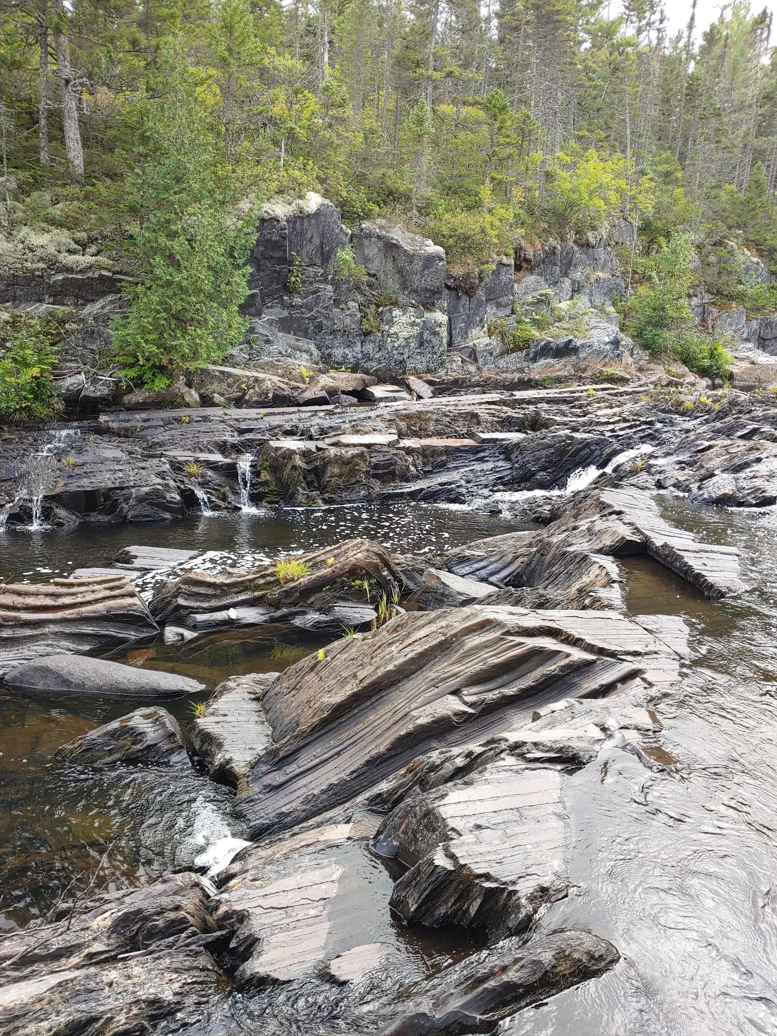Rocky riverbed with small waterfalls and layered dark rocks under natural light.