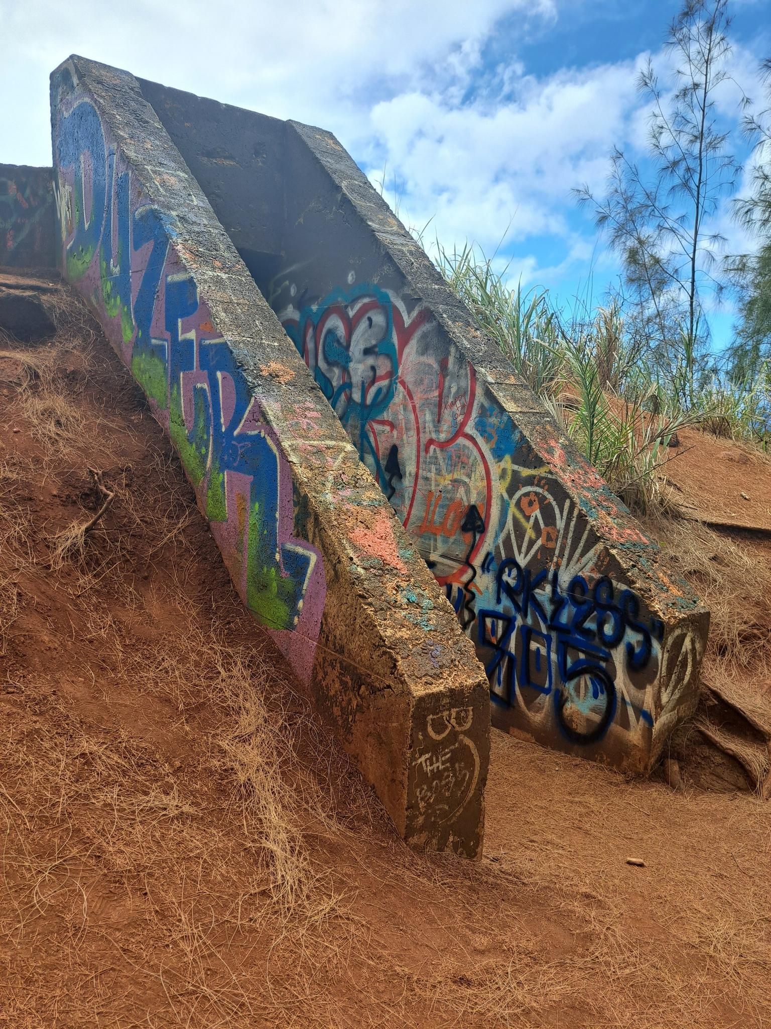Concrete structures covered in colorful graffiti on a reddish dirt hill. - Pu'uwaihu'ena loop