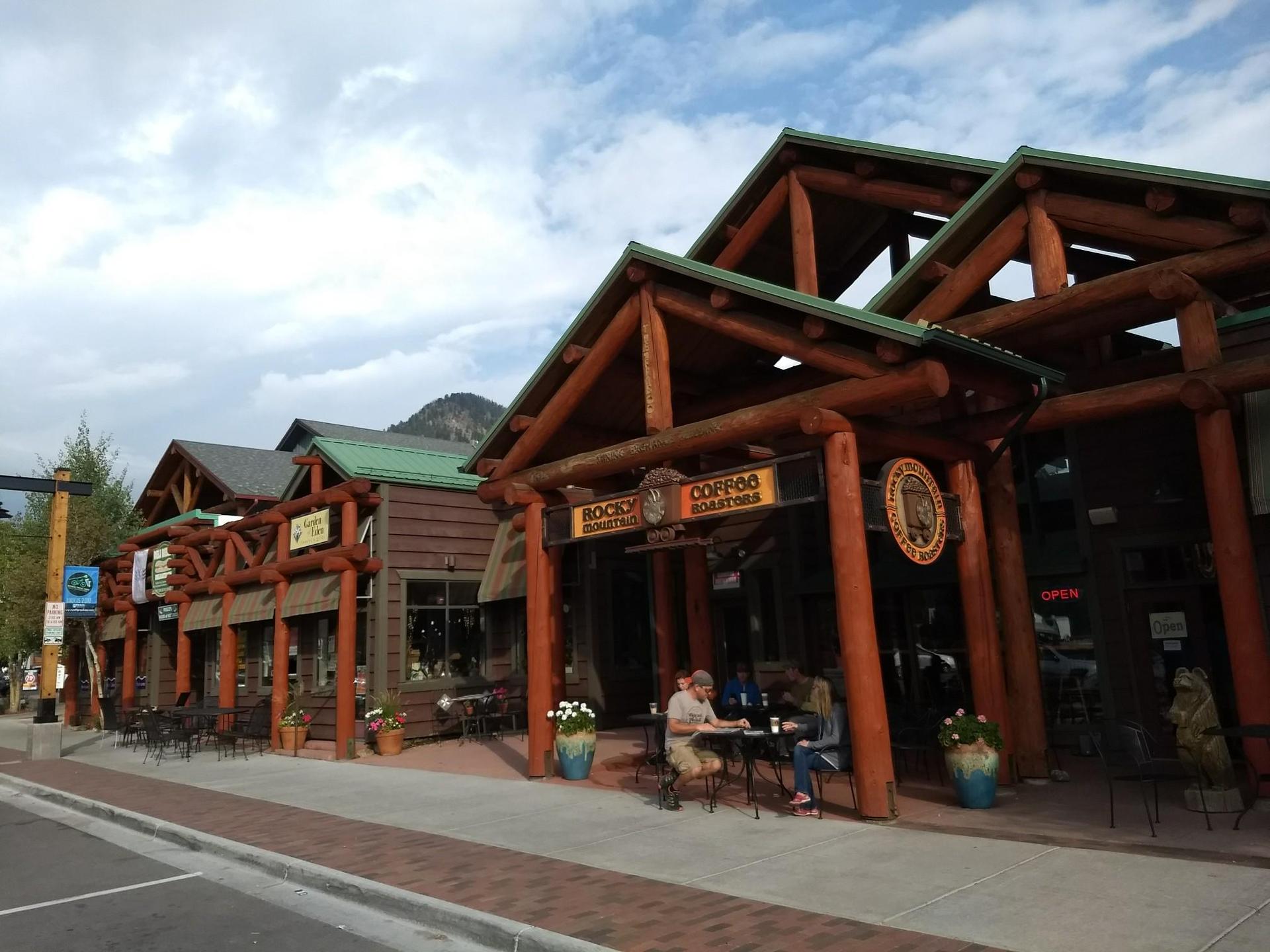 People sit outside rustic log cabin buildings on a cloudy day.