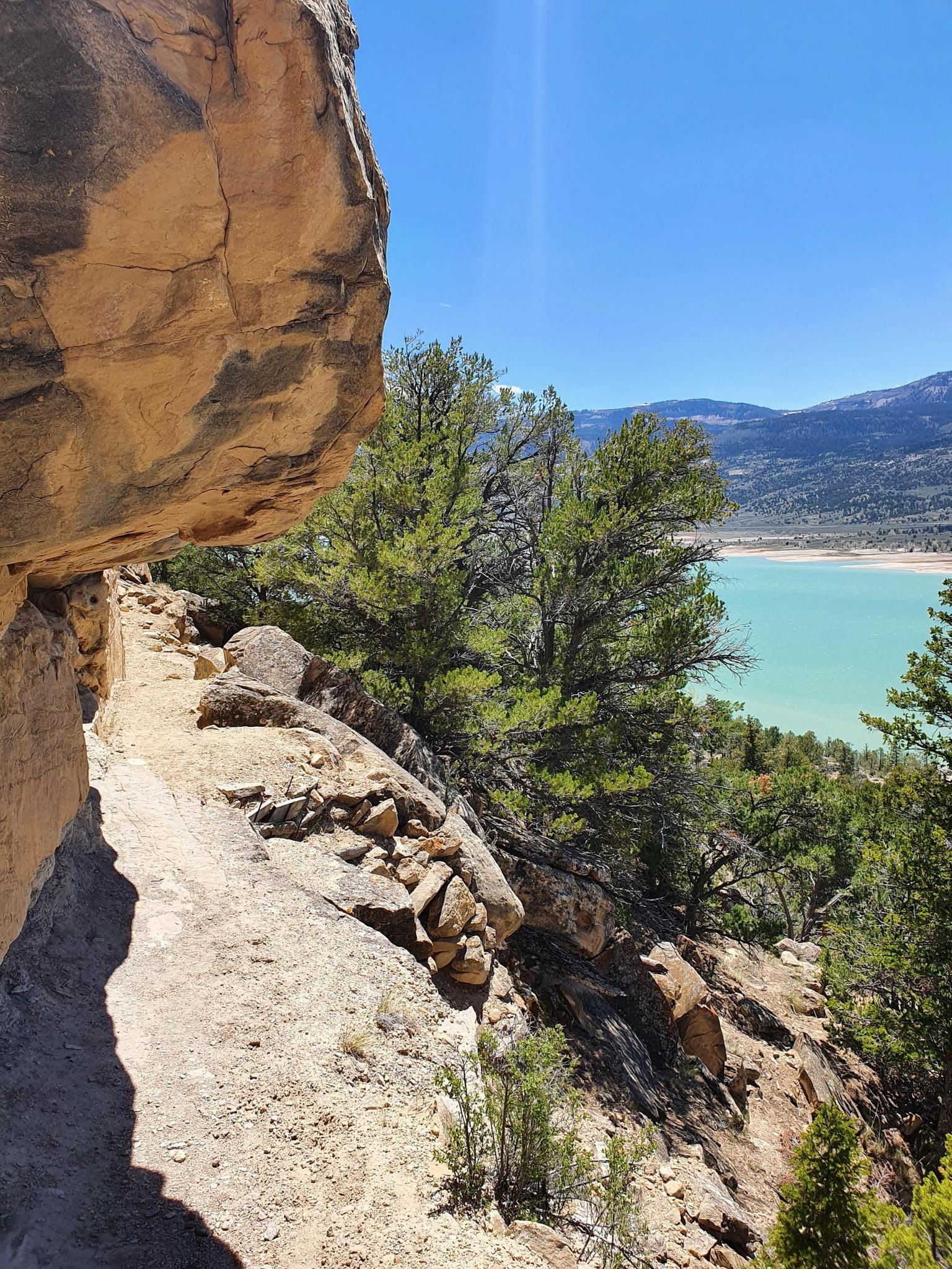 A narrow trail hugs a rock face overlooking a bright turquoise lake.