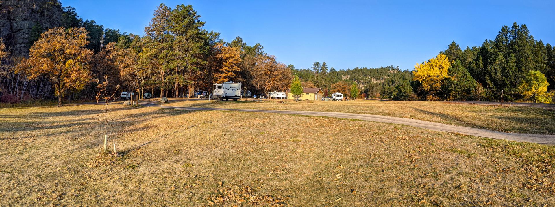 RVs parked in a wide, dry field with colorful autumn trees.