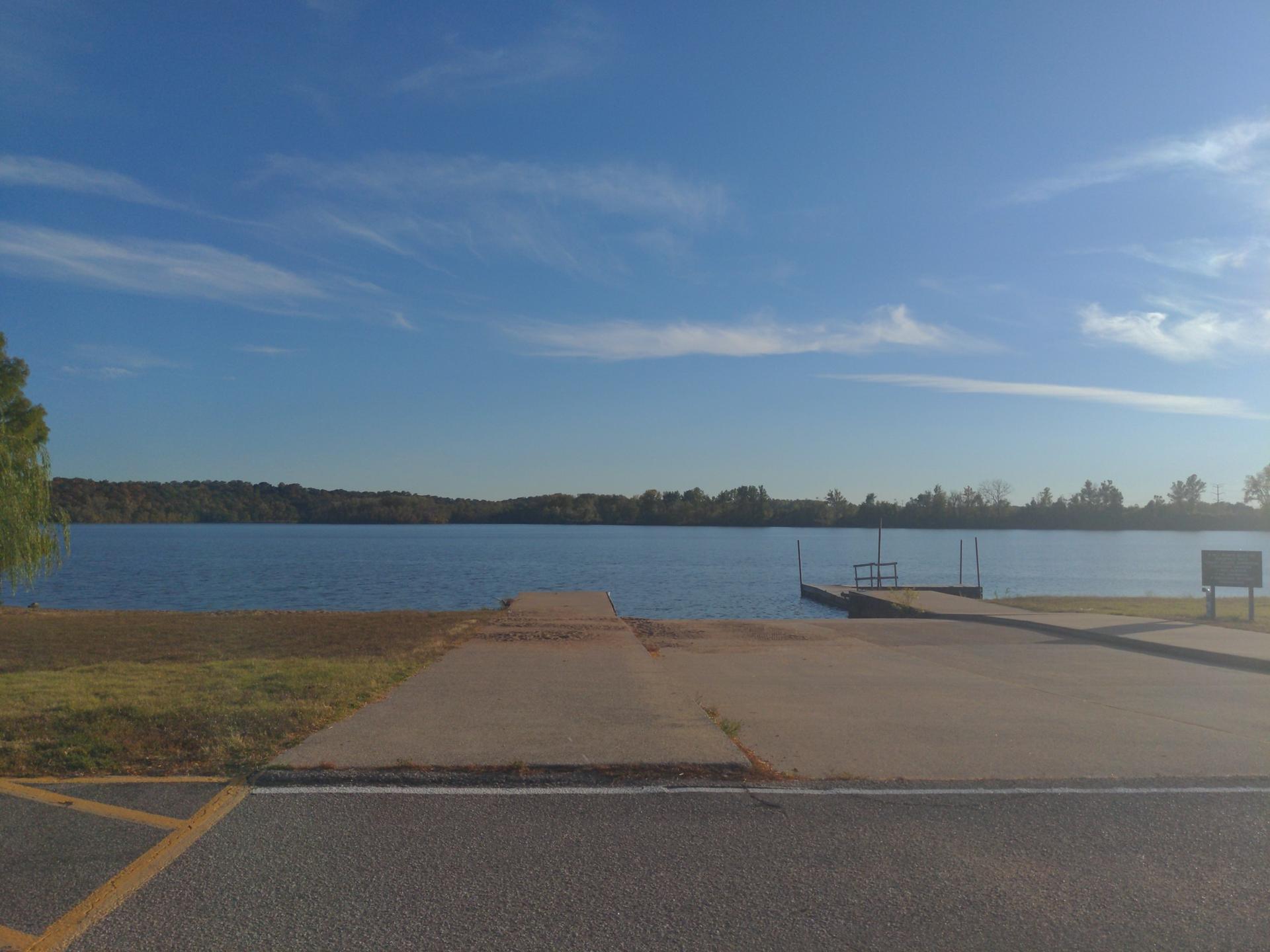 A boat ramp extends into a calm lake under a clear blue sky.
