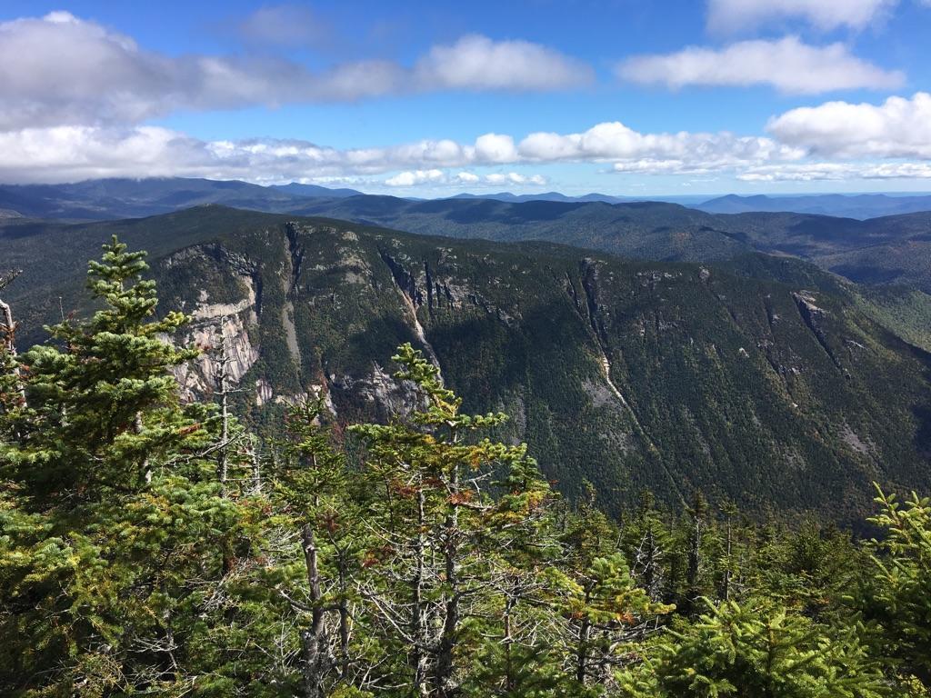 Panoramic view of forested mountains under a partly cloudy blue sky.
