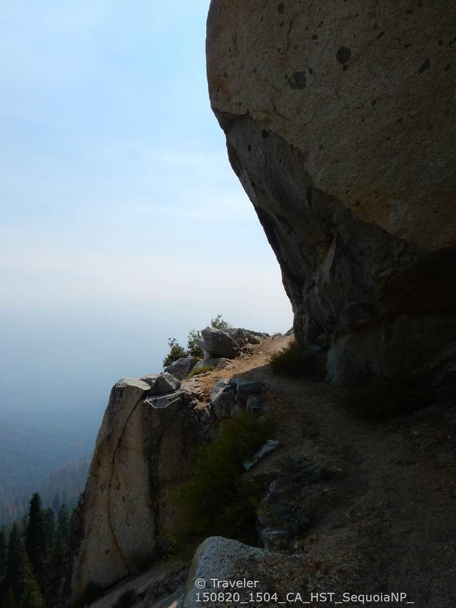 Narrow path clinging to a massive rock face with a hazy distant view.