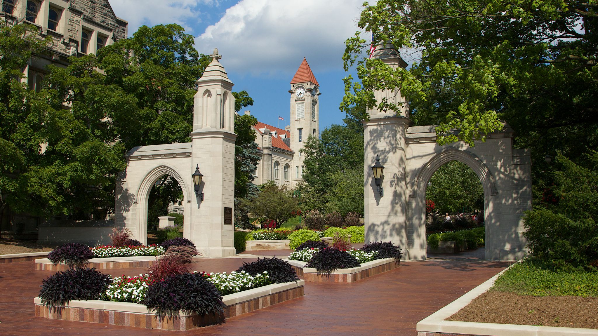 Ornate stone archways frame a distant castle-like building with a red roof, surrounded by green trees and gardens. - Lake Monroe loop from Bloomington