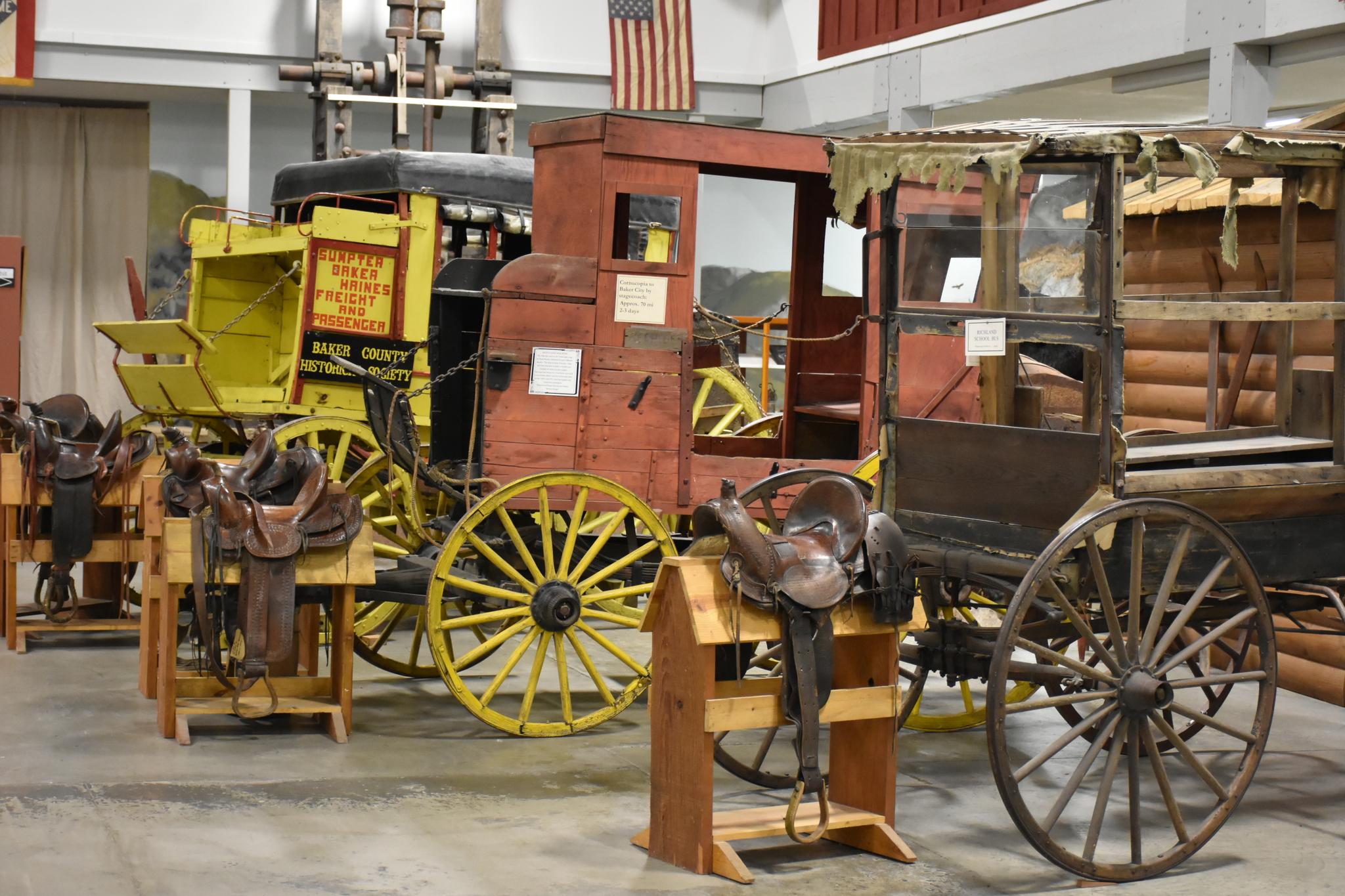 Historic carriages and saddles displayed indoors, under artificial lighting.