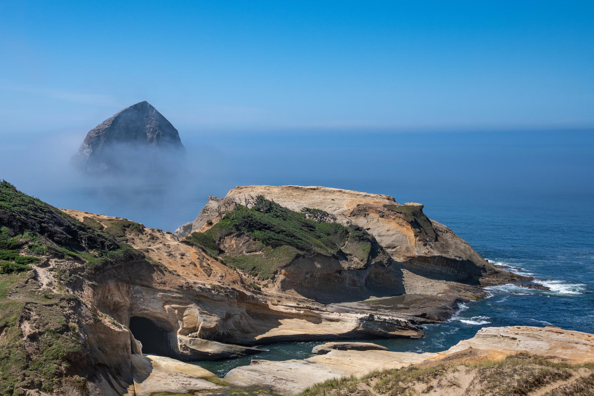 Rocky coastline with sea caves, ocean, and a large sea stack in fog.
