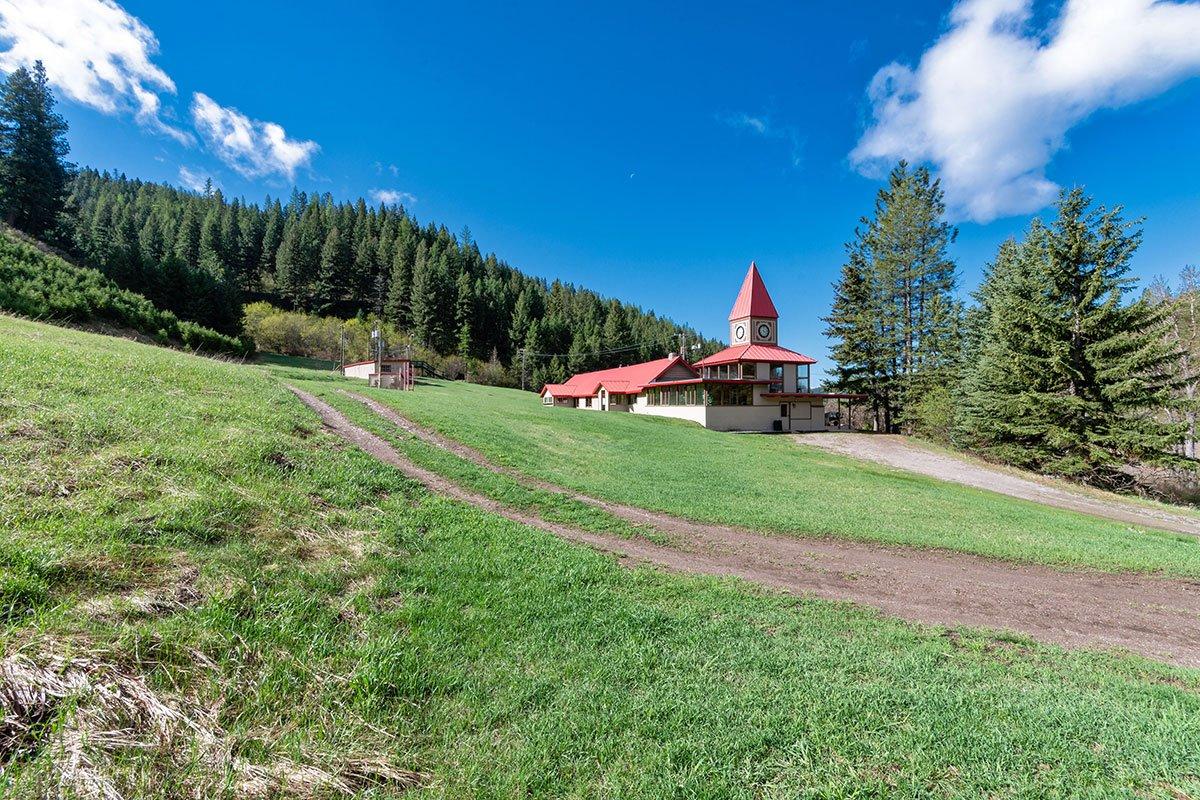 A distinctive building with a red roof and clock tower on a sunny, green hillside.