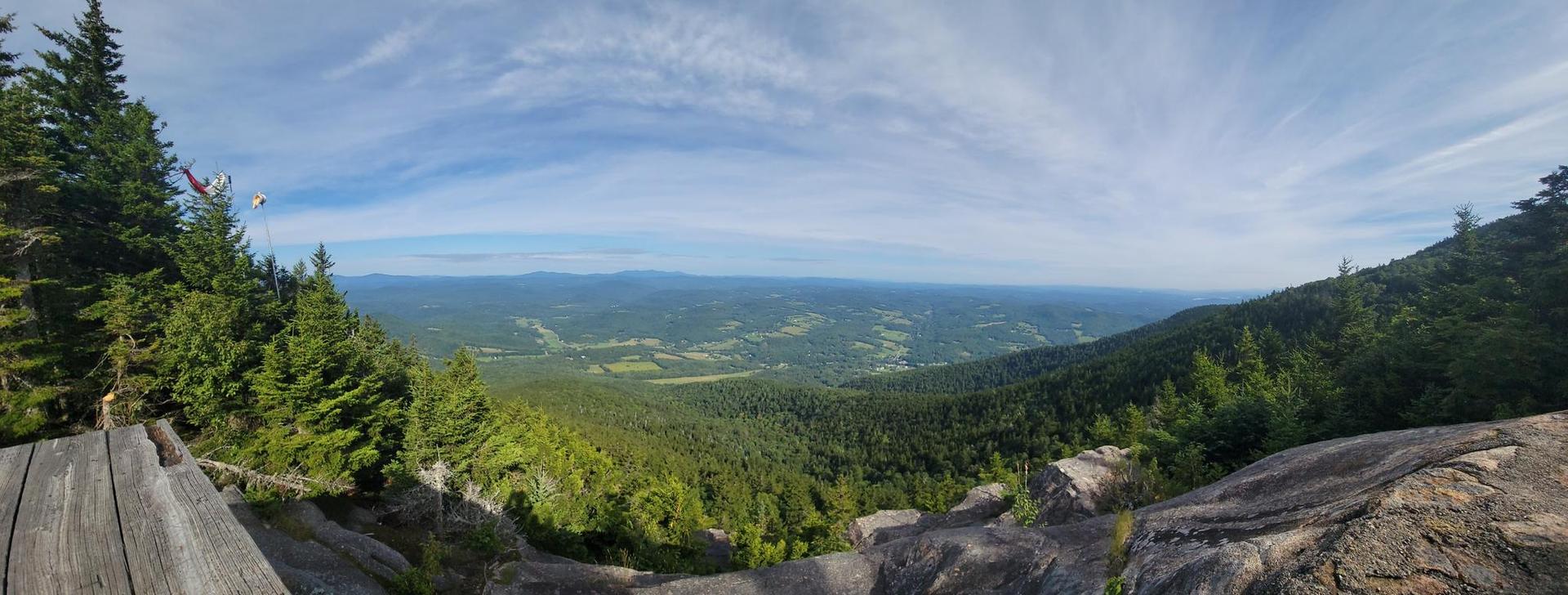 Panoramic view of a vast green valley and distant mountains under a blue sky.