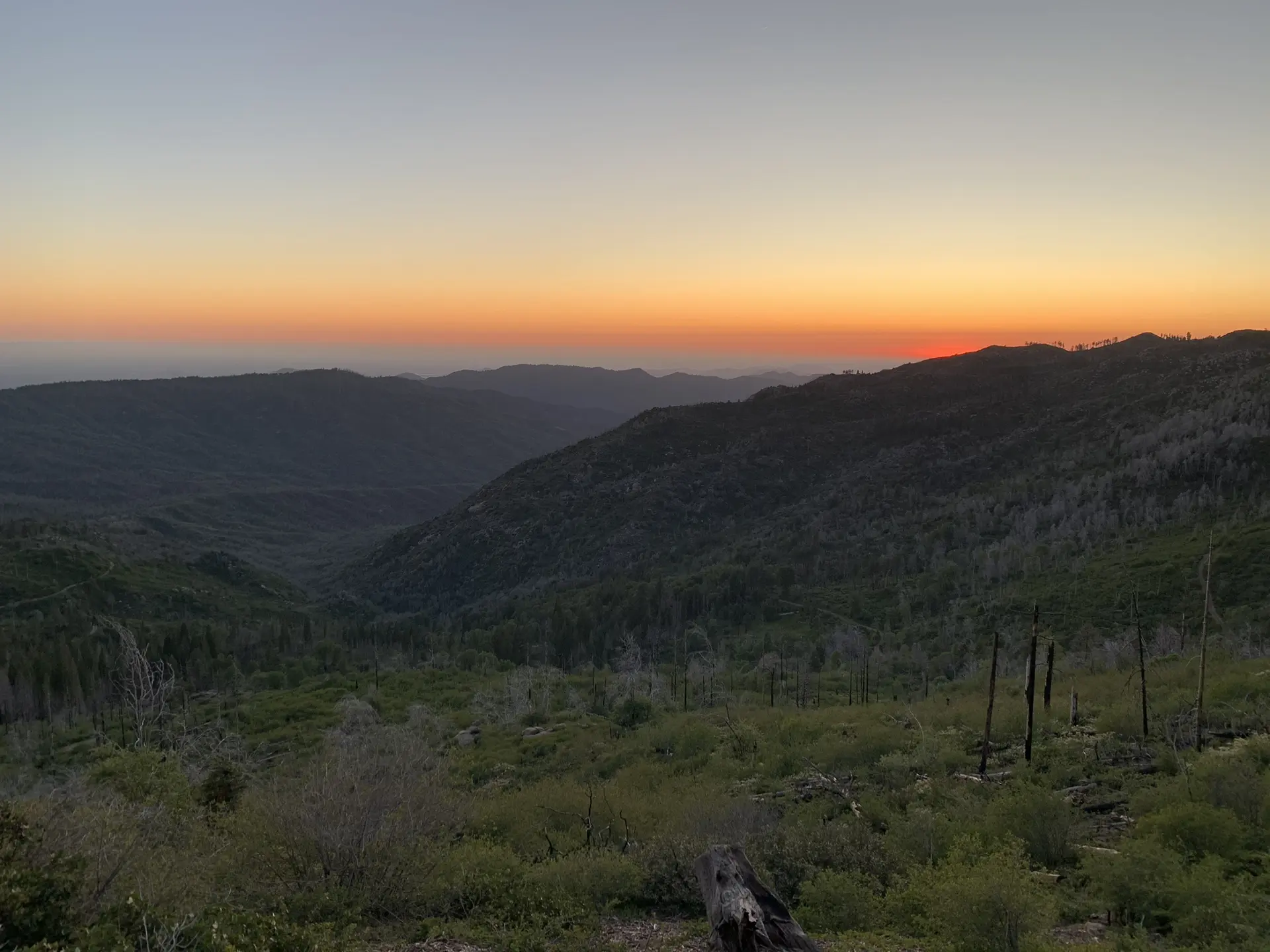 Mountainous landscape at sunset, with an orange glow on the horizon.