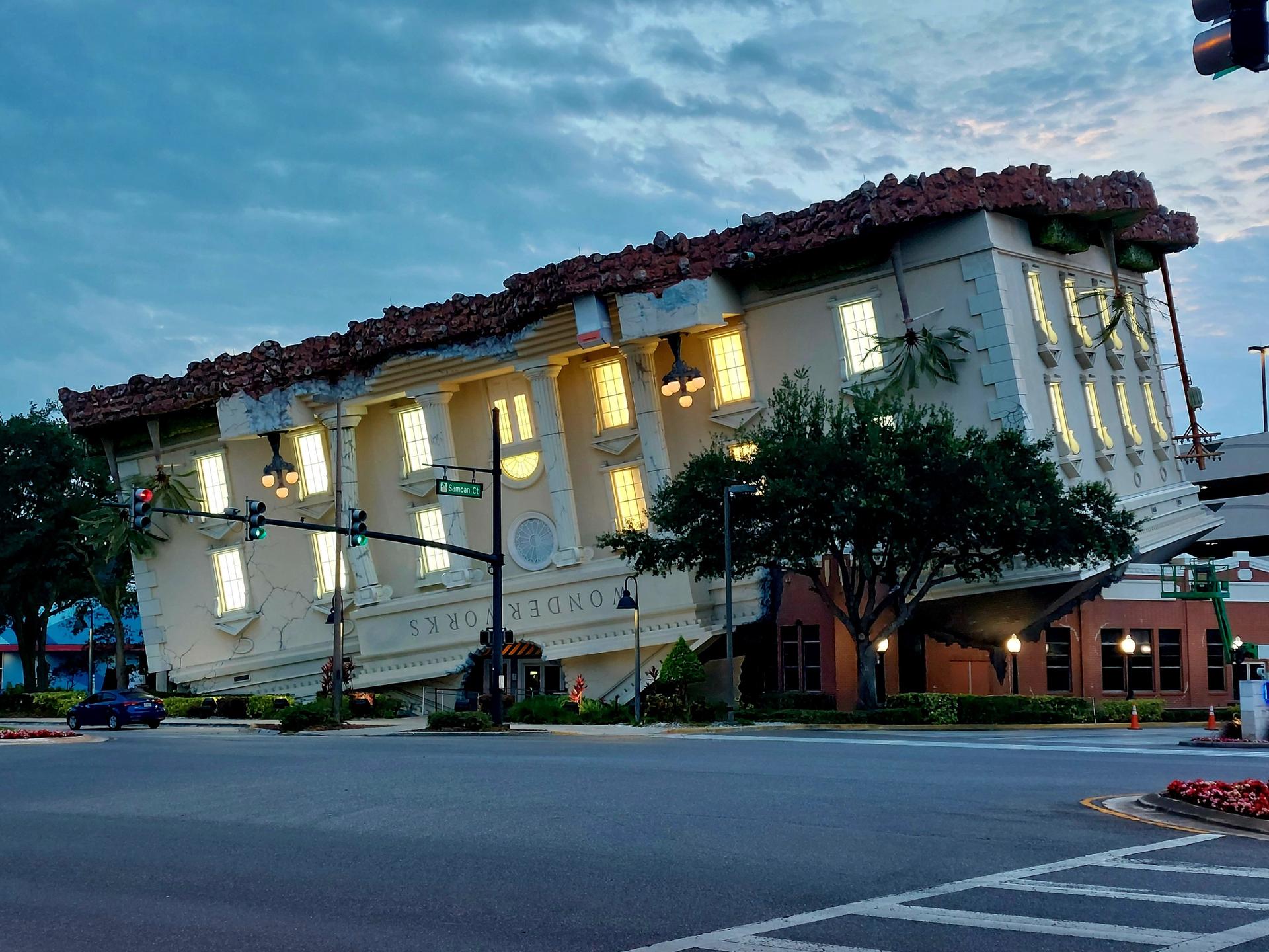An unusual, large building appearing upside-down at dusk with lights on.