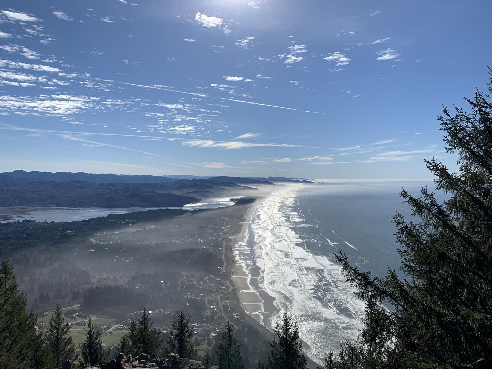 Bright, expansive coastal view of a long beach, ocean, town, and distant mountains.
