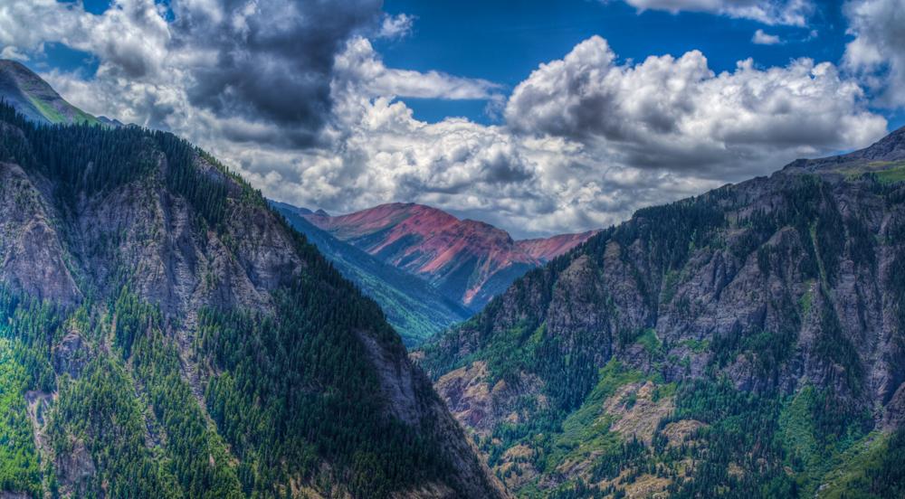 Dramatic mountain valley with forested slopes under a cloudy sky.