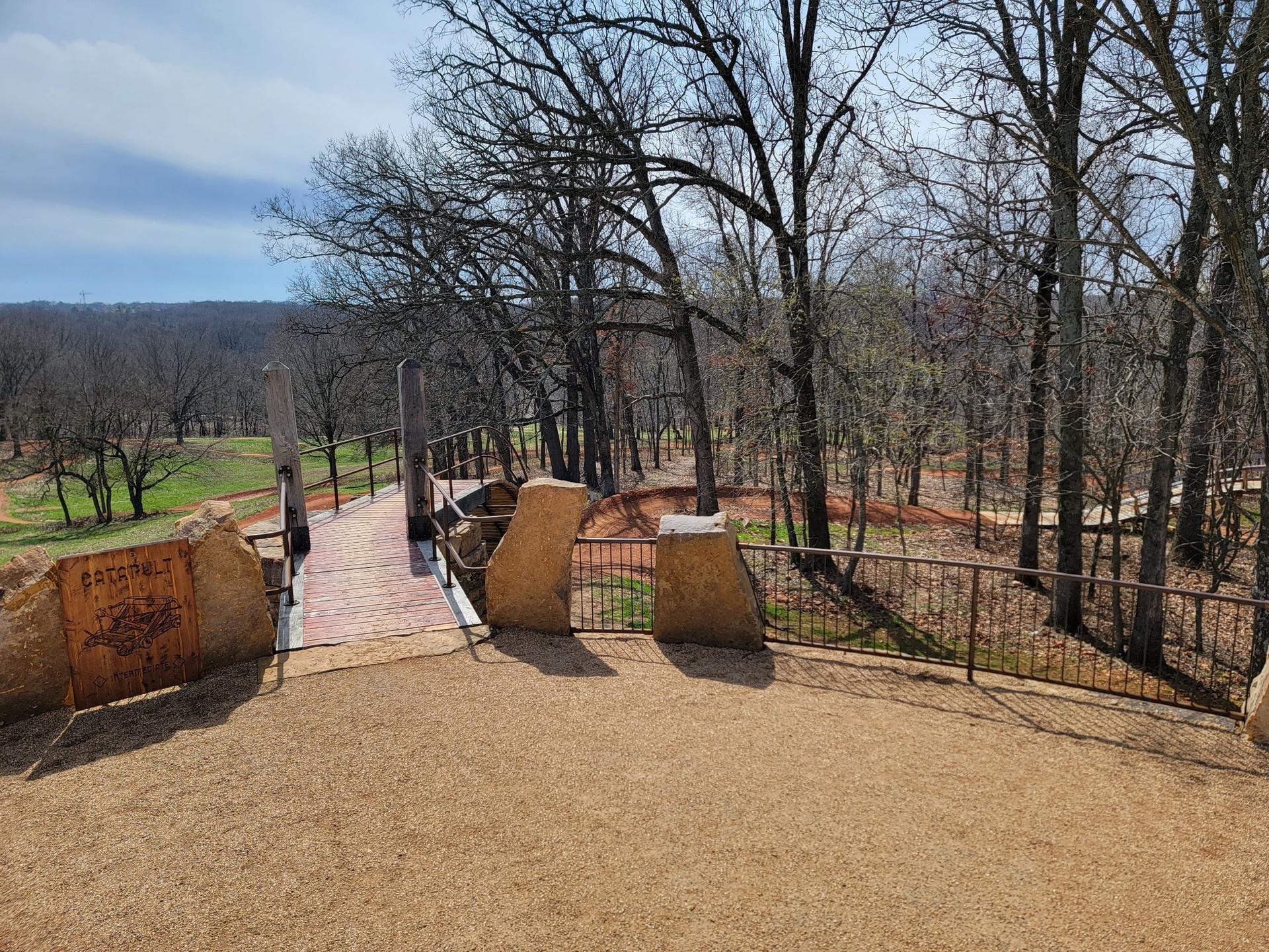 Elevated wooden bridge overlooking a vast landscape with bare trees.