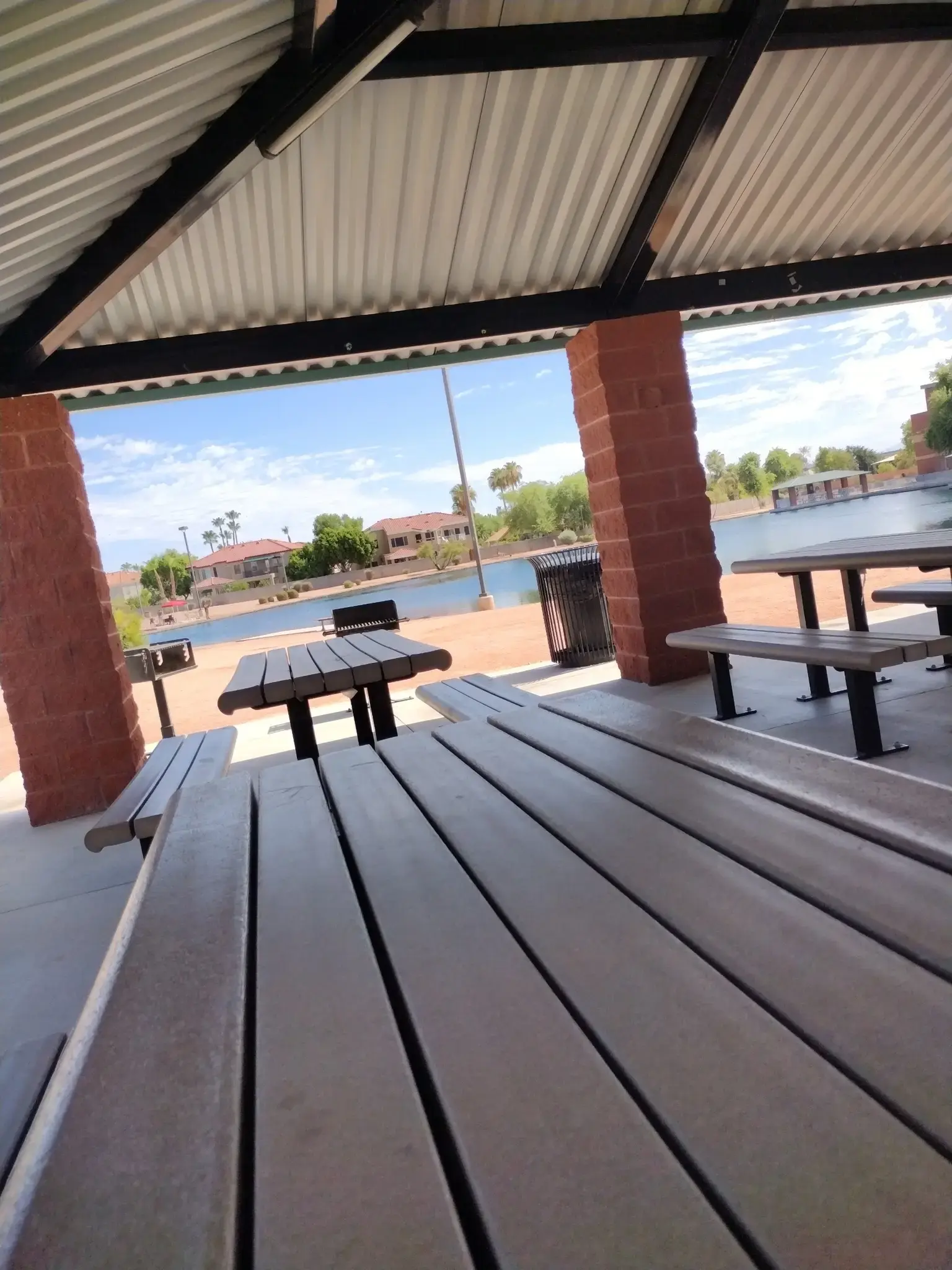 Picnic tables under a shelter by a lake on a bright, sunny day.