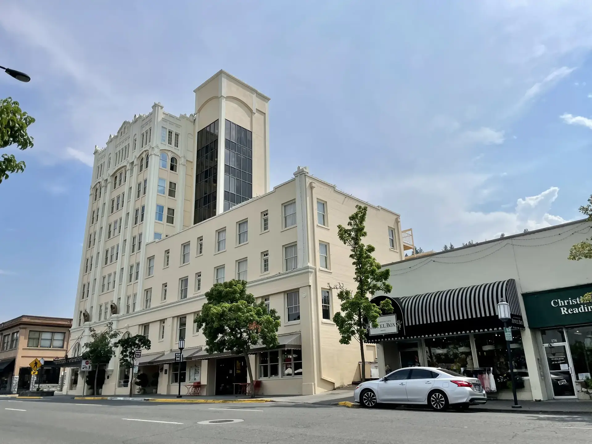 A tall, light-colored building on a city street with shops and cars.