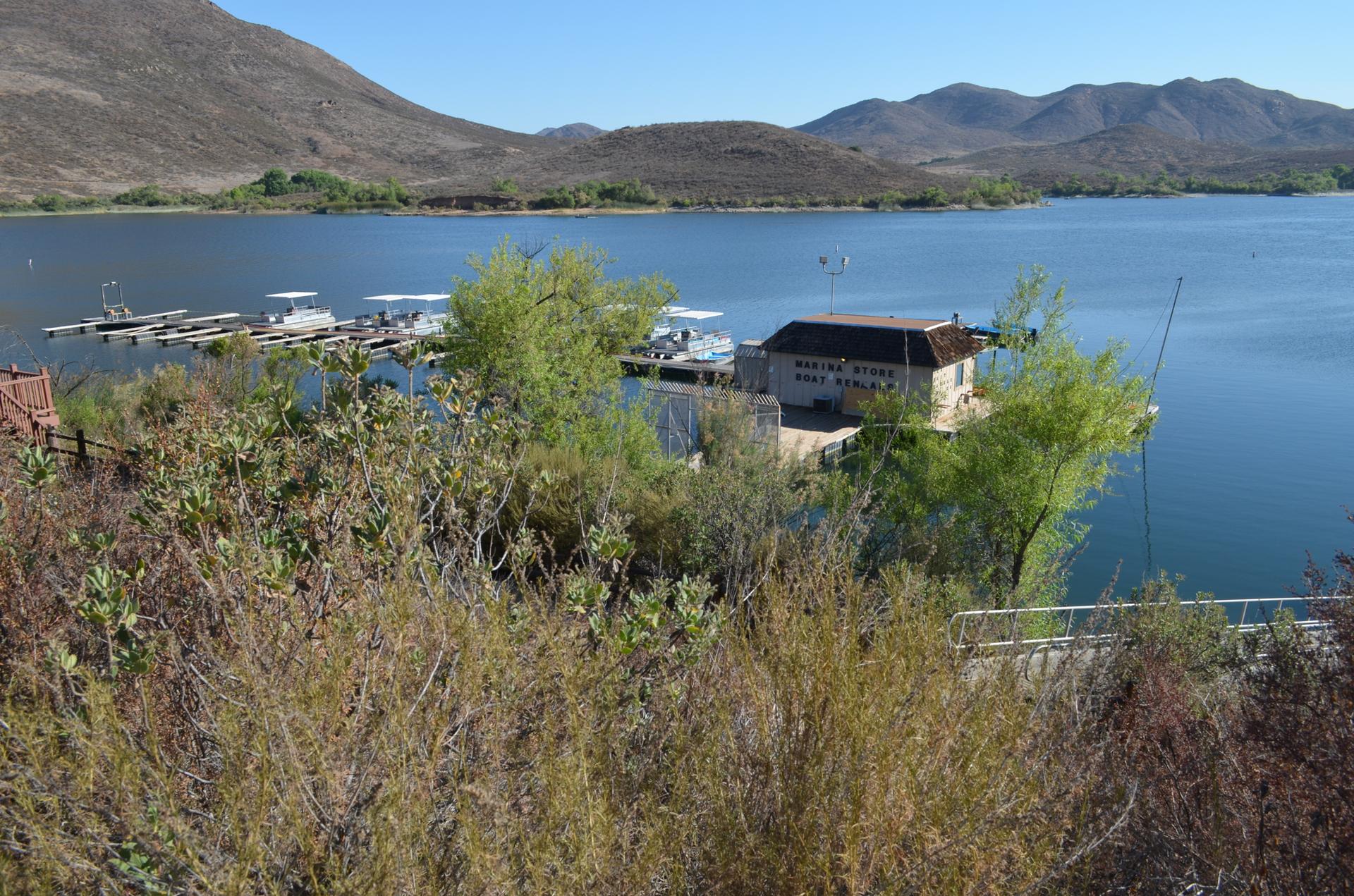 Sunny view of a lake with a building, docks, boats, and distant mountains.