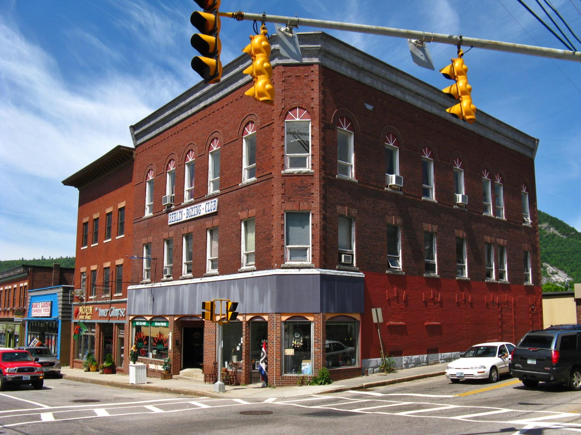 Large brick building at a sunny street intersection with traffic lights.