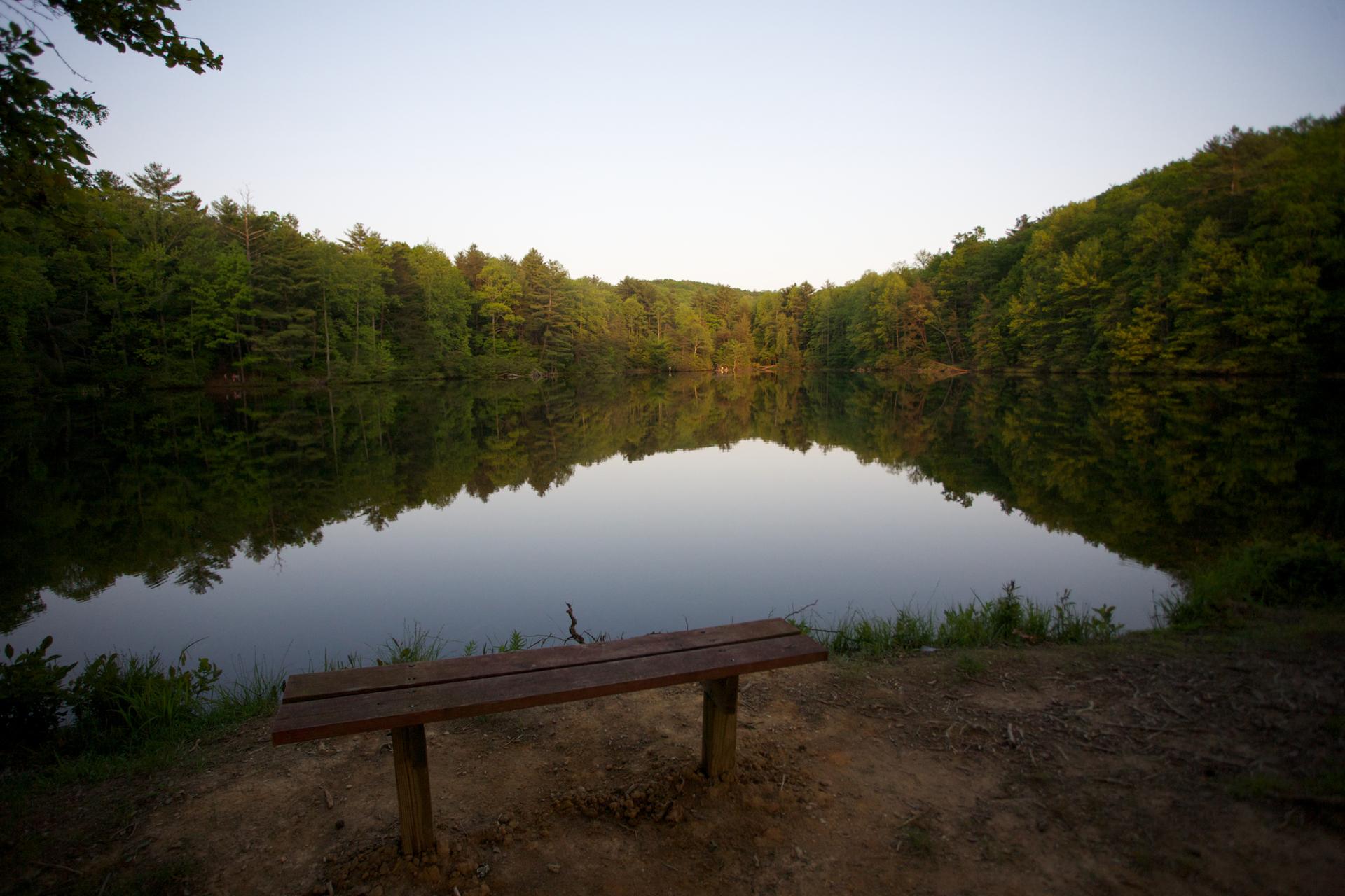 Wooden bench overlooking a calm lake reflecting forested hills at dusk.