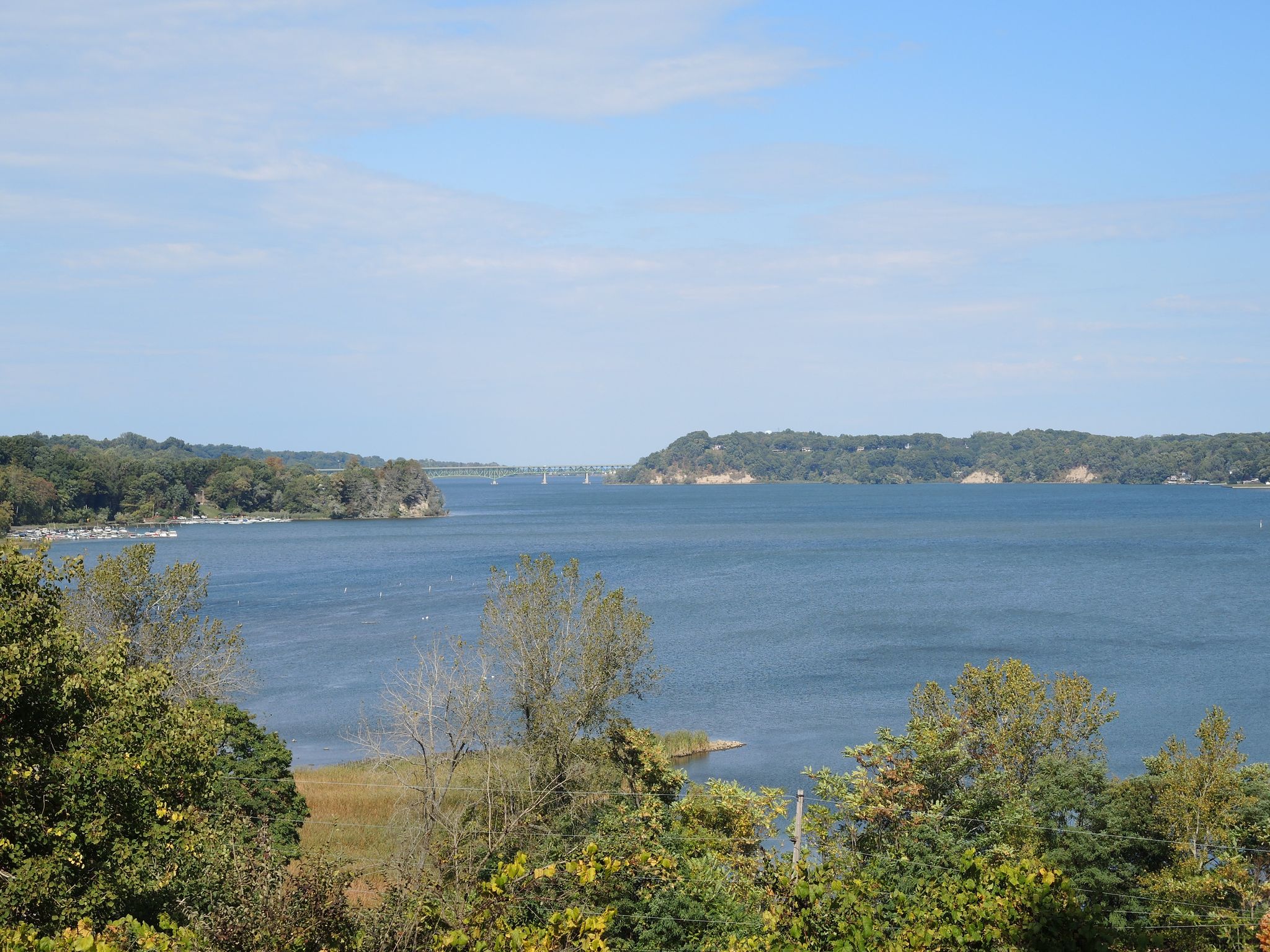Panoramic view of a wide bay surrounded by green trees under a bright sky. - Irondequoit Bay loop