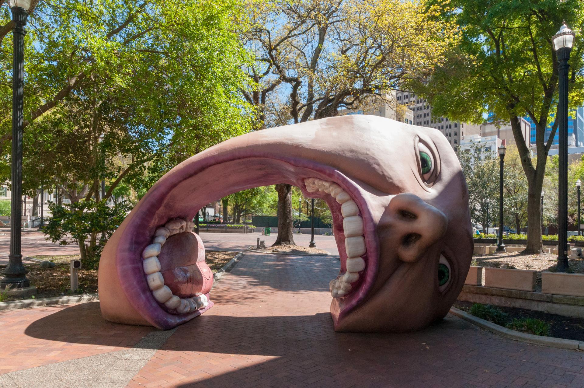 Large, whimsical head sculpture with open mouth archway in a sunny park.