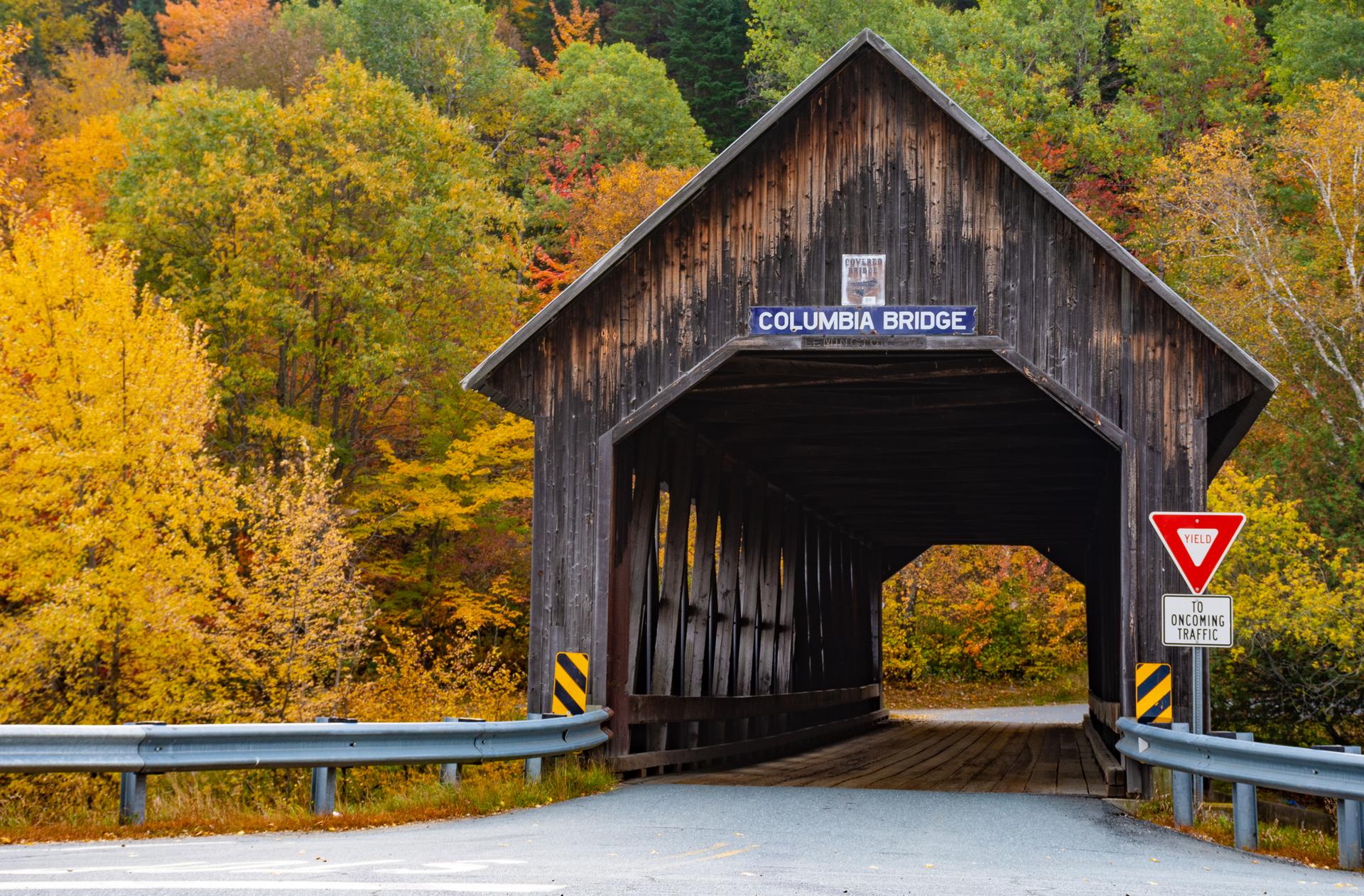 A rustic wooden covered bridge surrounded by vibrant autumn foliage.