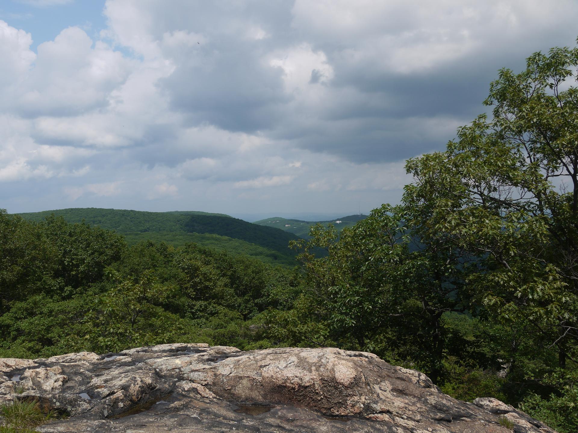 View of rolling green forested hills under a cloudy sky from a rocky outcrop.