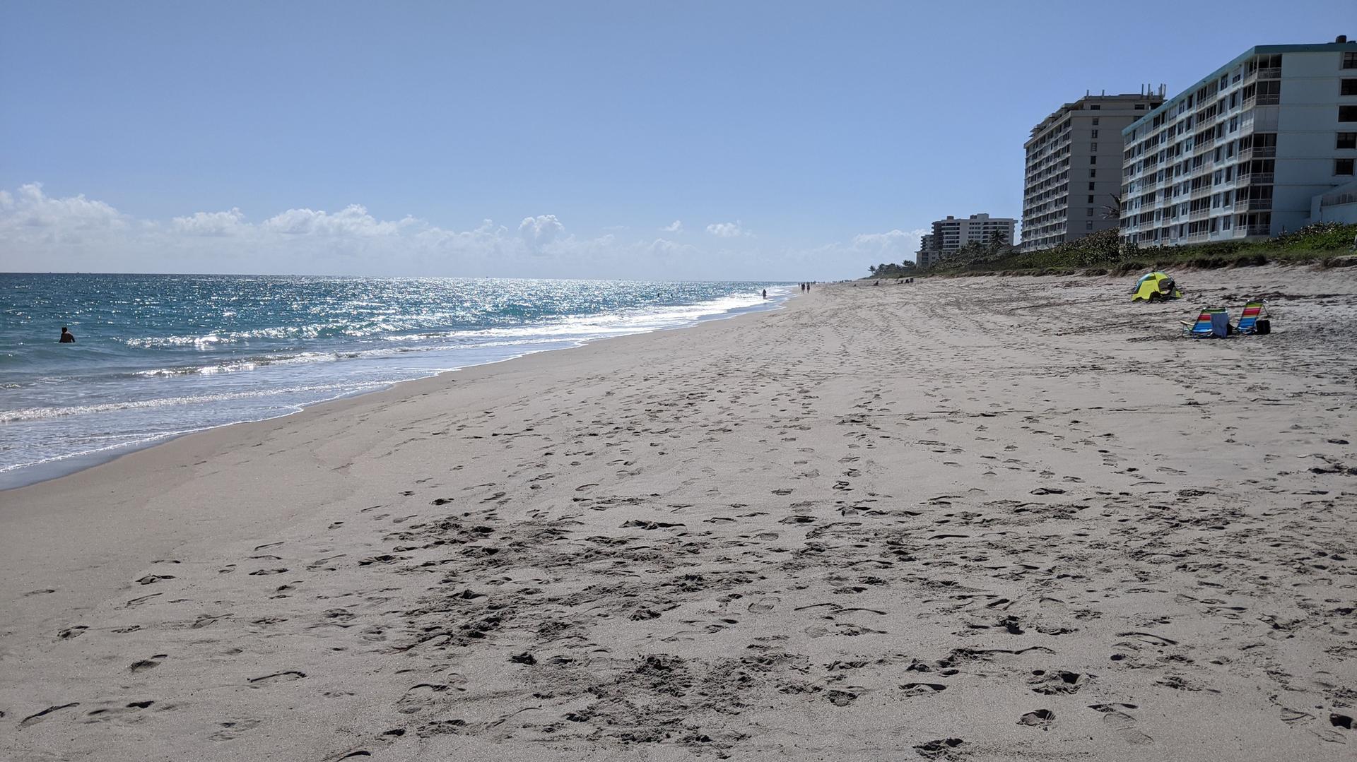 Expansive sandy beach with ocean waves, distant buildings, and people enjoying the sun.
