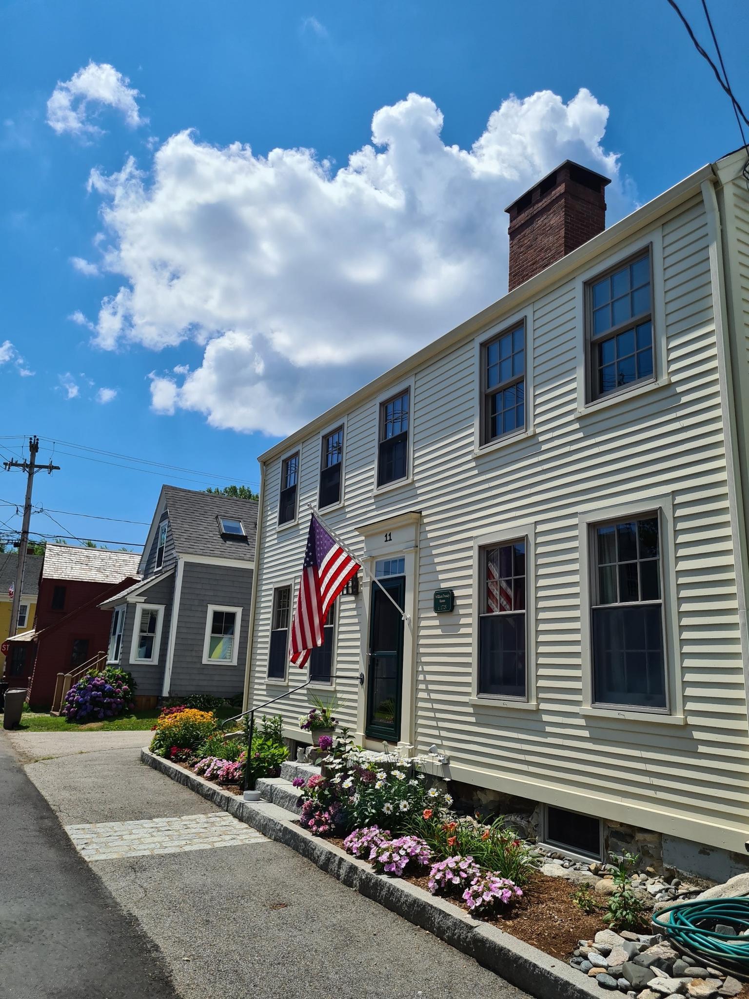 A light-colored house with an American flag and flower beds on a sunny day.