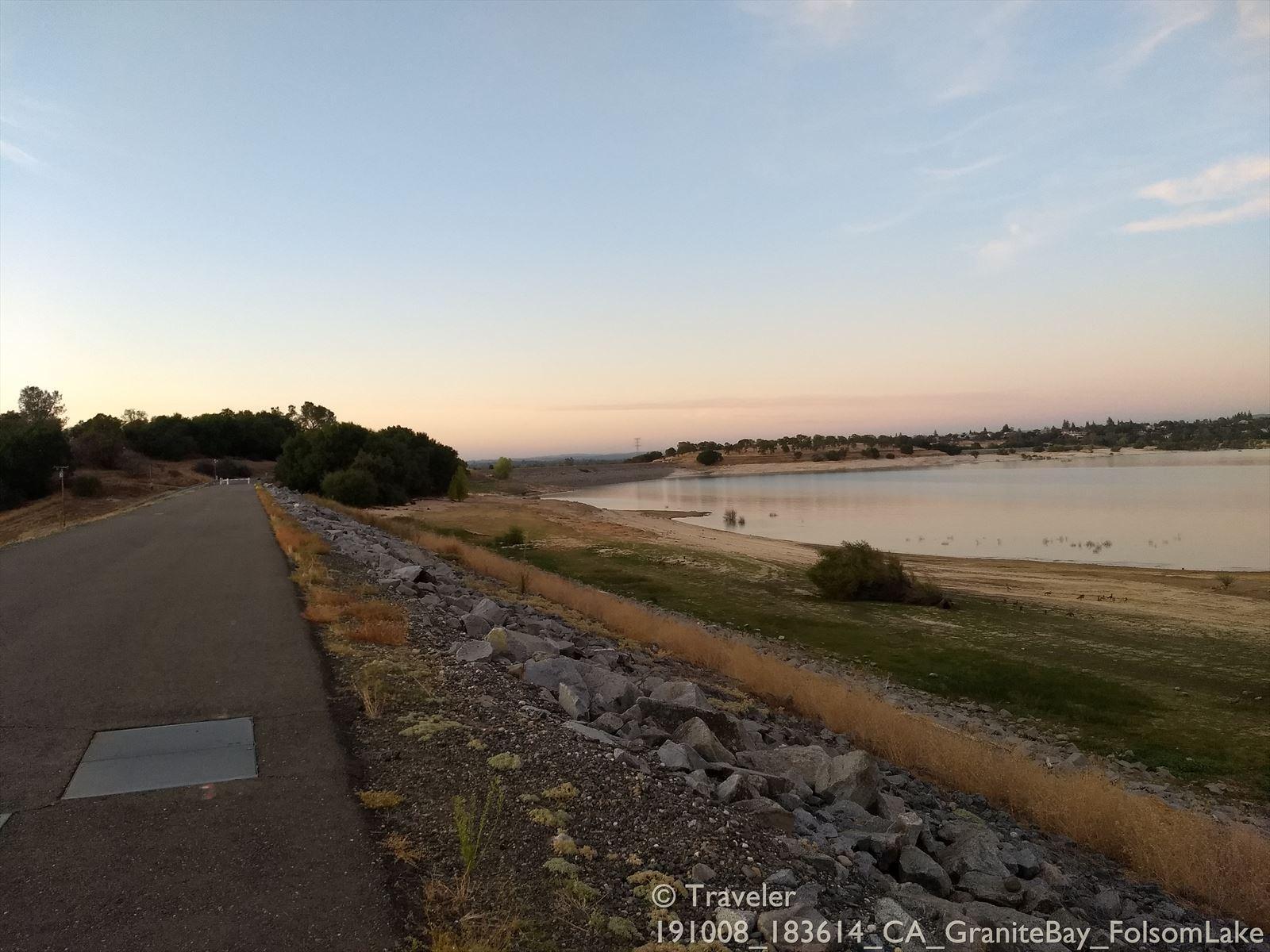 A paved road next to a lake with dry grass and scattered rocks.