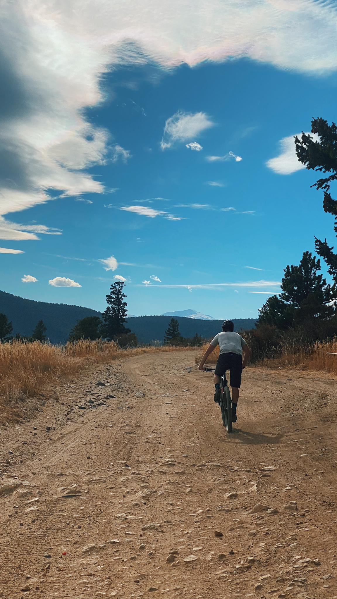 A person cycles on a dirt road under a cloudy blue sky.
