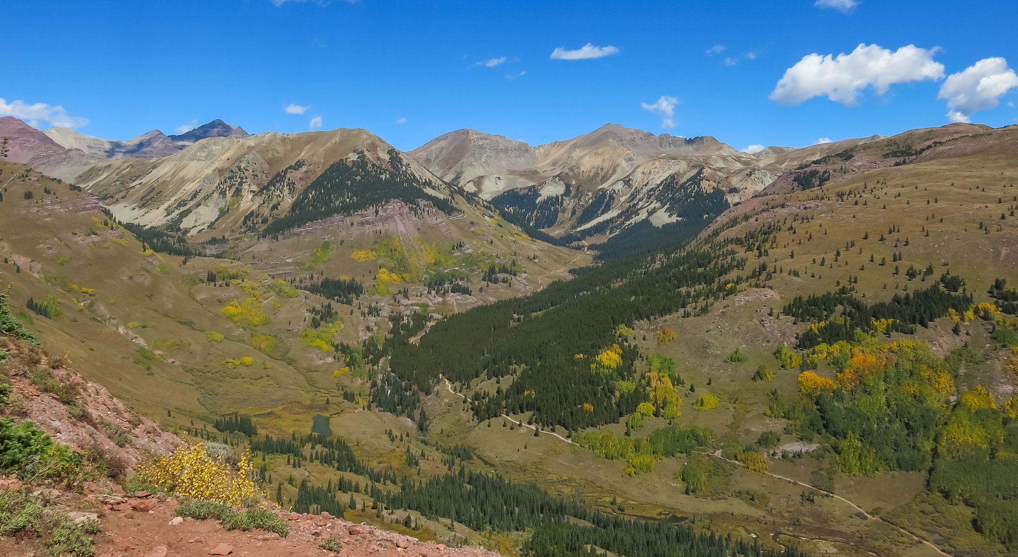 Panoramic view of a vast mountain range and valley with colorful autumn trees. - Teocalli Ridge Loop