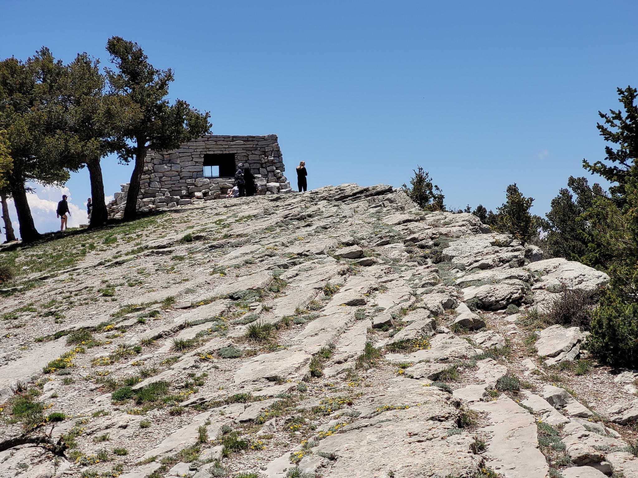 People exploring a rocky outcrop with a stone building under a clear blue sky.