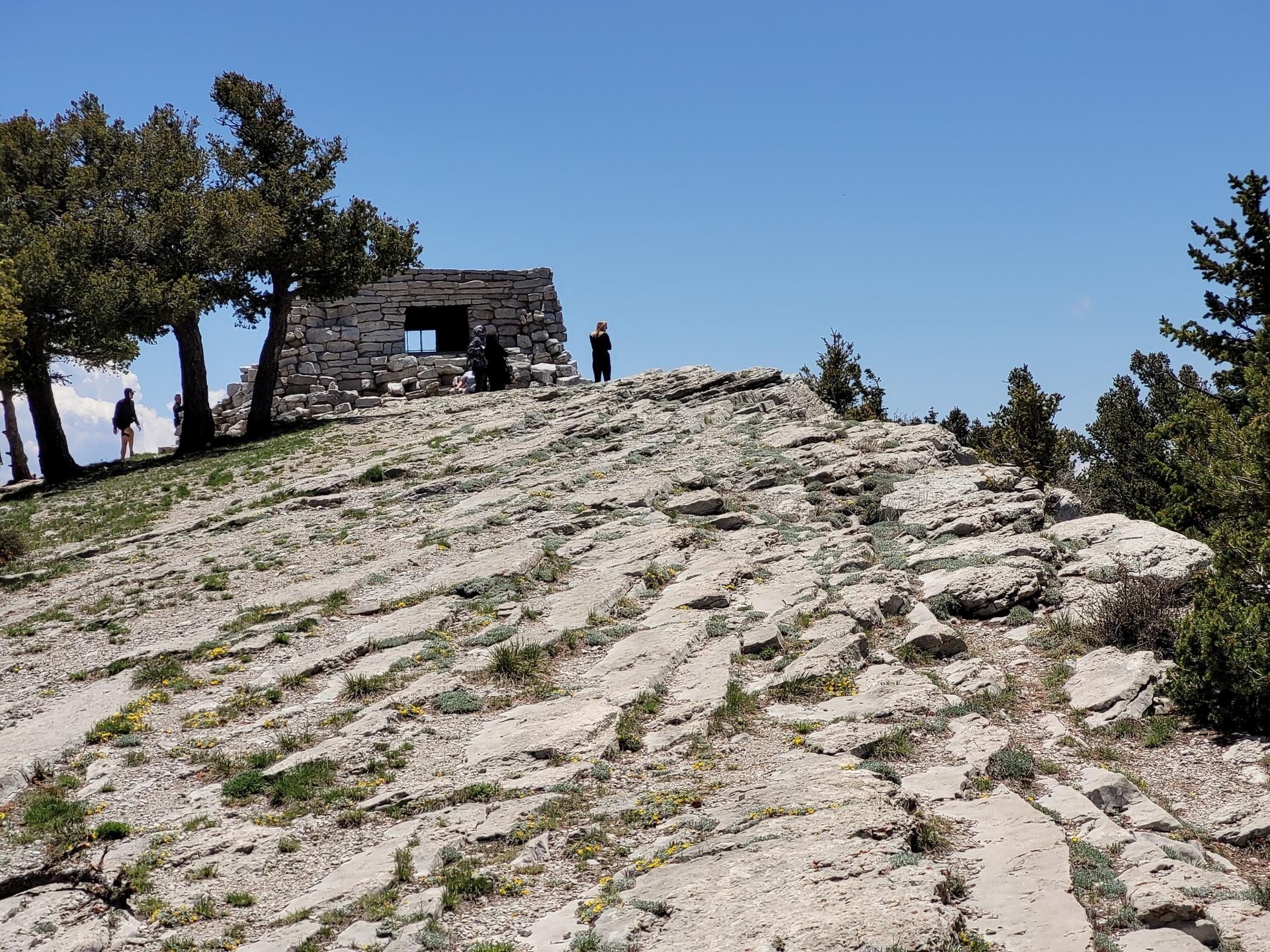 People exploring a rocky outcrop with a stone building under a clear blue sky.